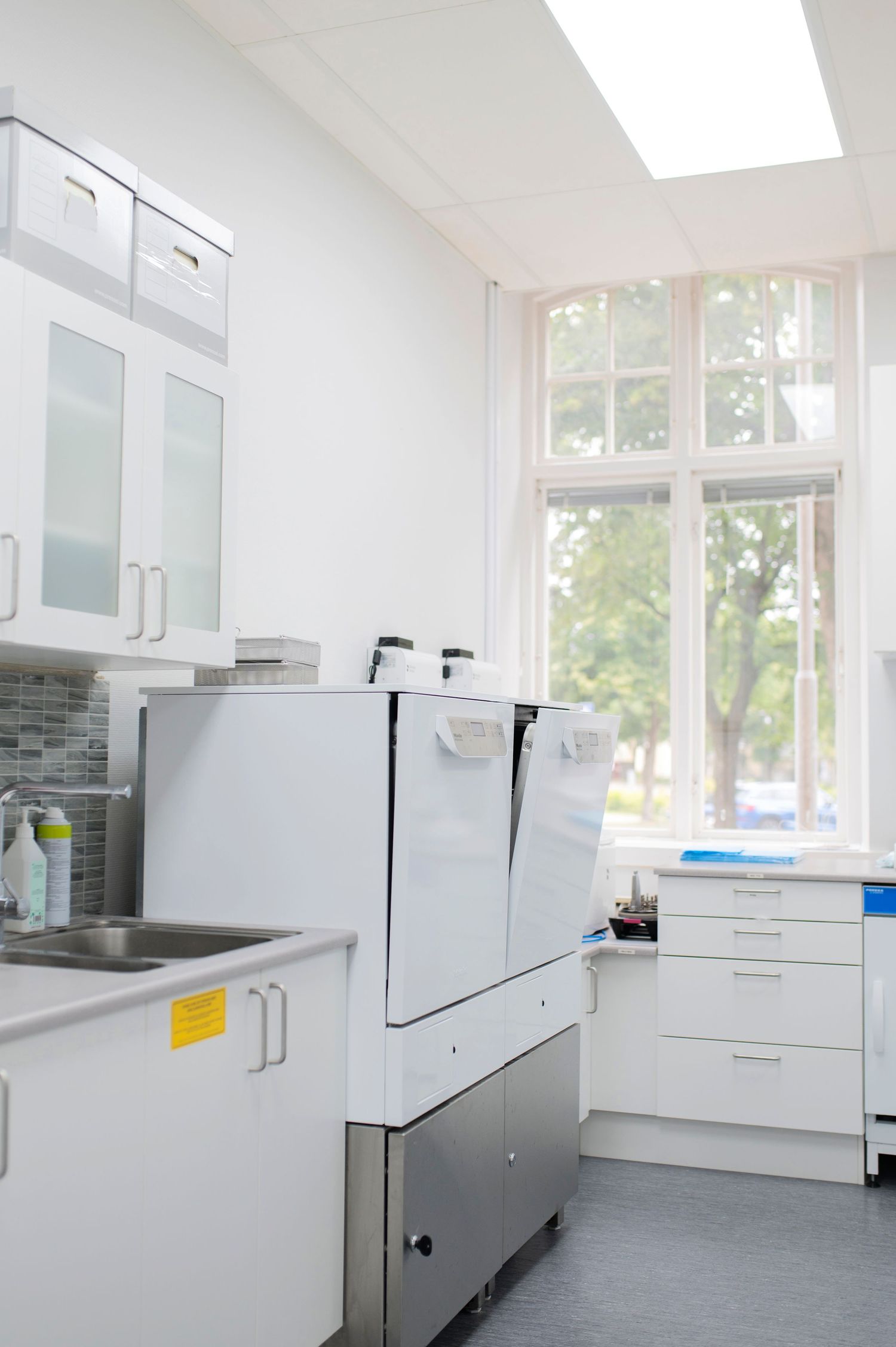 Modern white laboratory room with professional equipment, cabinets, and a large window overlooking green trees.