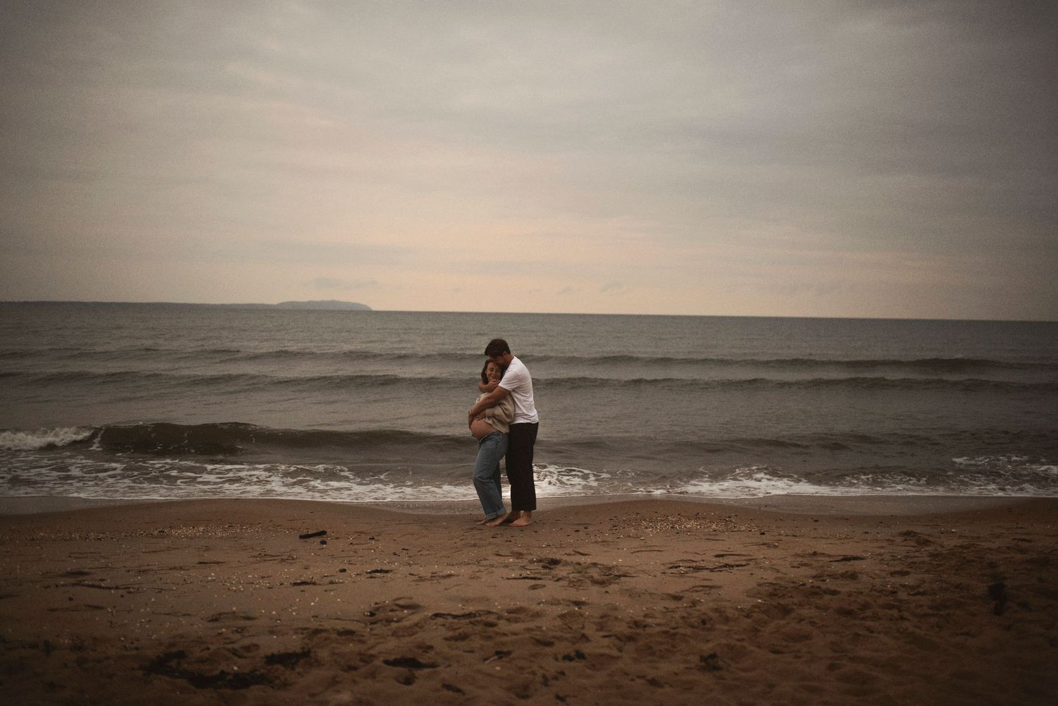 Silhouette of couple embracing on beach during golden hour with waves in background.