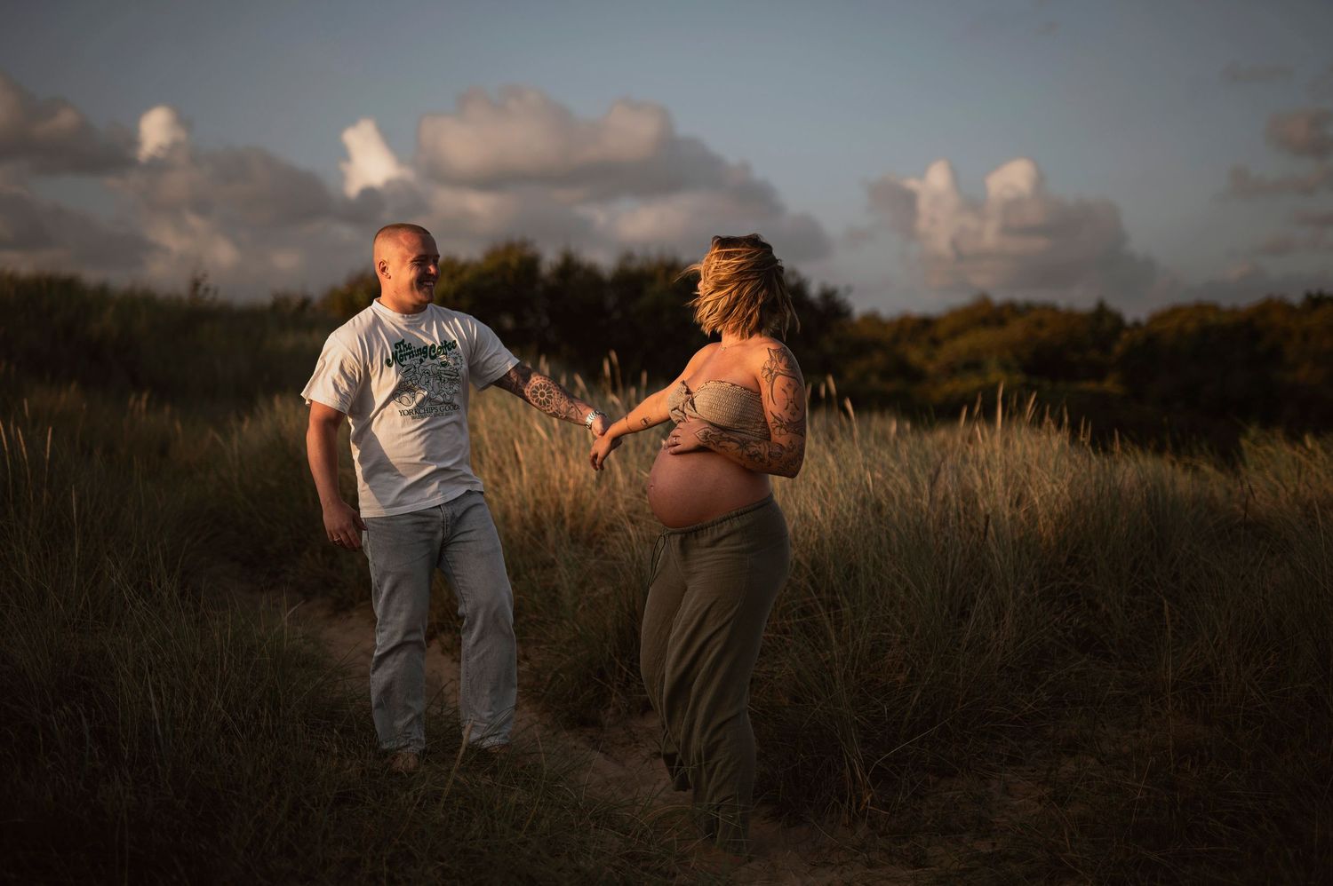 An intimate maternity session captures a couple dancing together at golden hour in a grassy field.