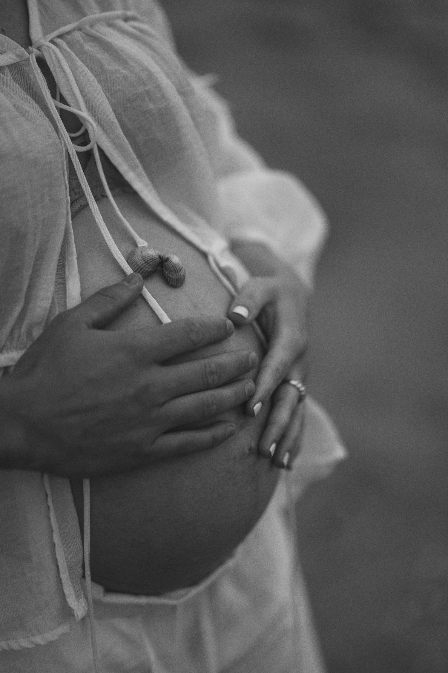 Close-up black and white photo of hands cradling a pregnant belly in a sheer dress.