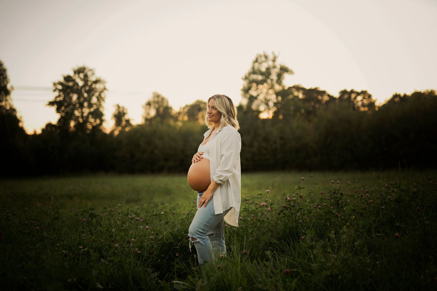 Side profile maternity photo in a meadow with golden hour lighting.