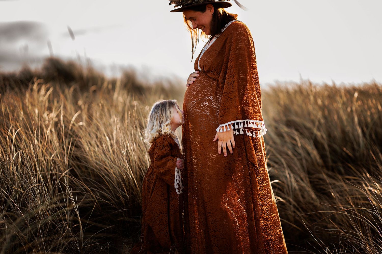 Sweet moment between parent and child in matching rust-colored dresses amid tall prairie grass.