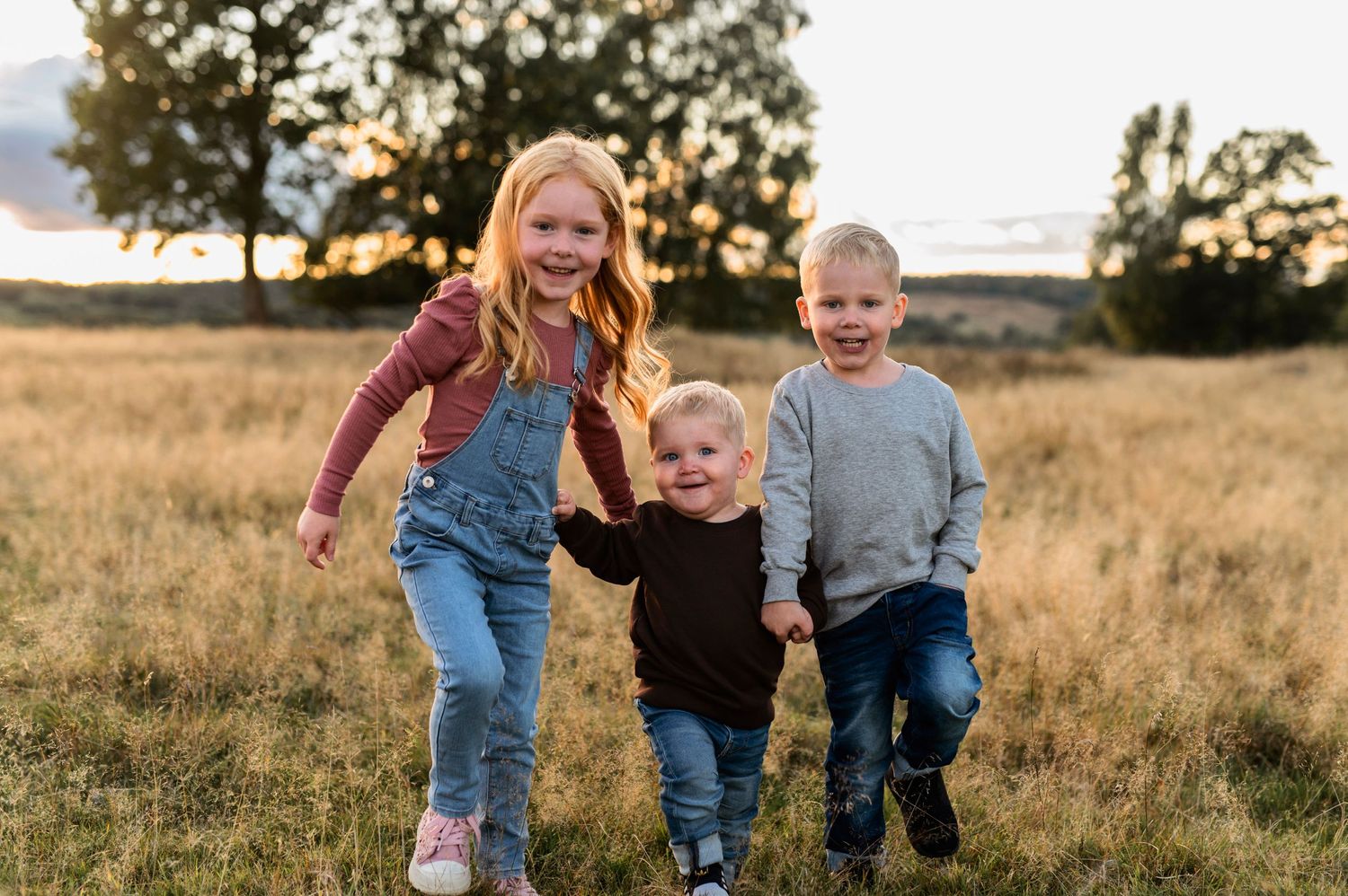 Three children running and playing together in a golden field at sunset.