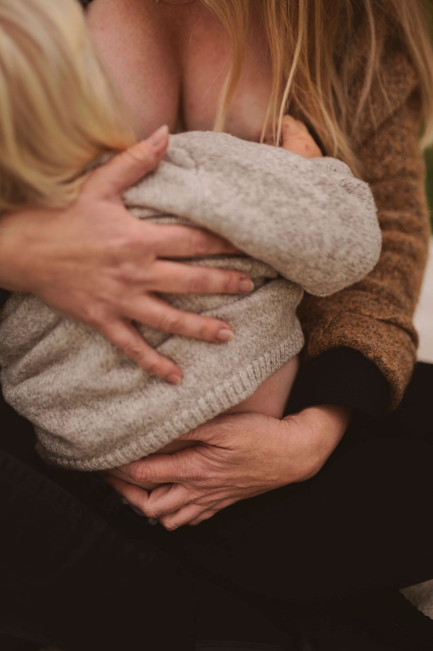 Close-up detail of hands holding small child in grey sweater during feeding.