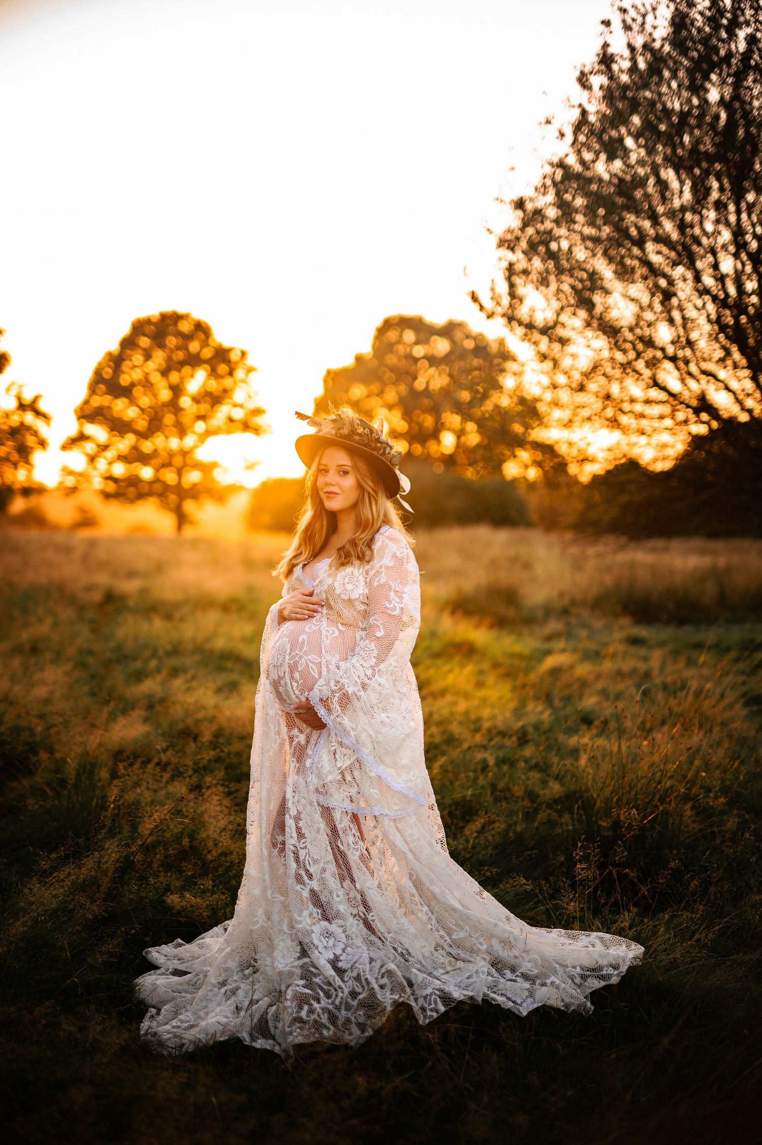 Romantic maternity portrait in flowing white lace dress during golden hour sunset.