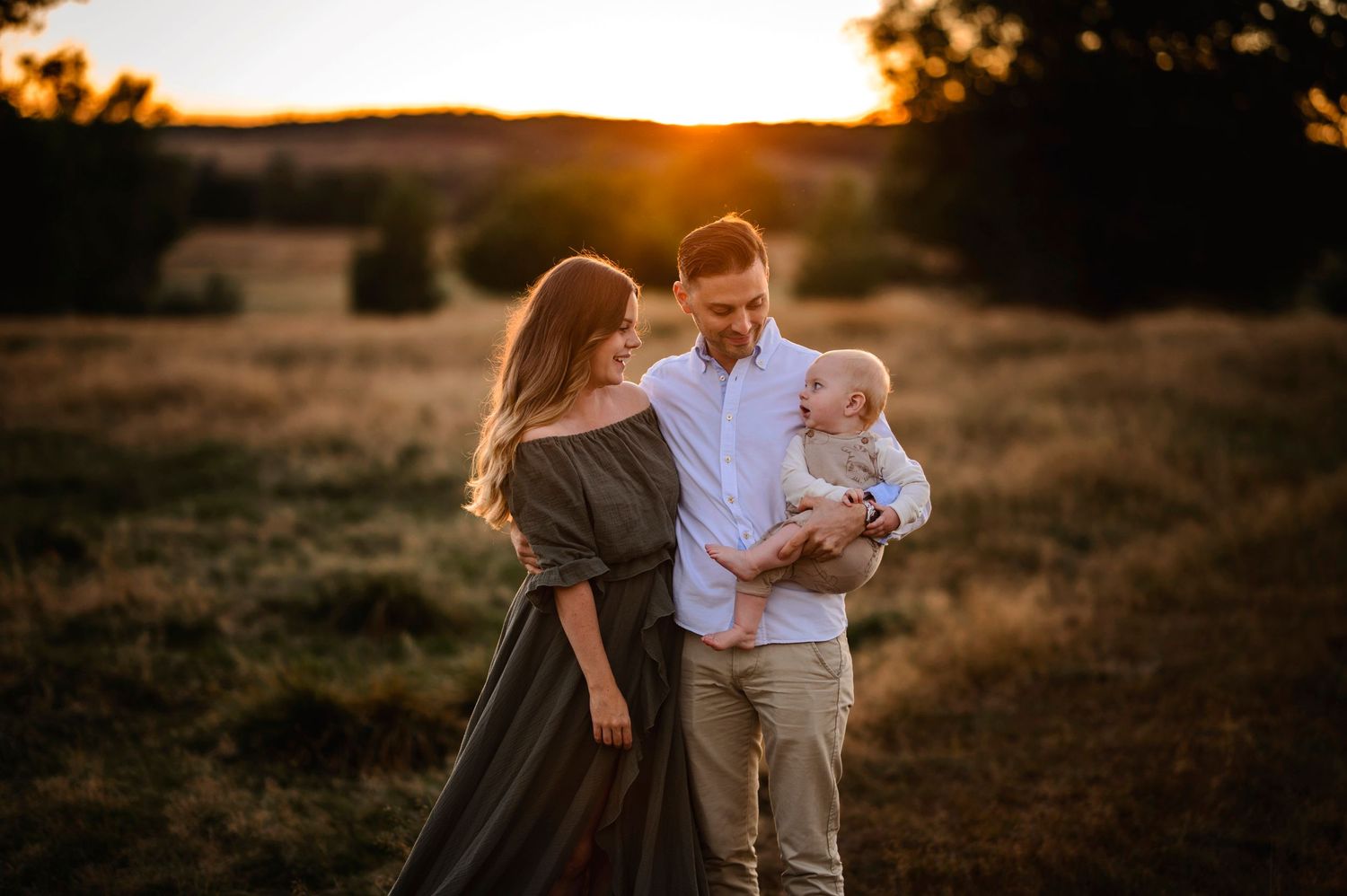 A family of three shares an intimate moment in a sunset-lit field.