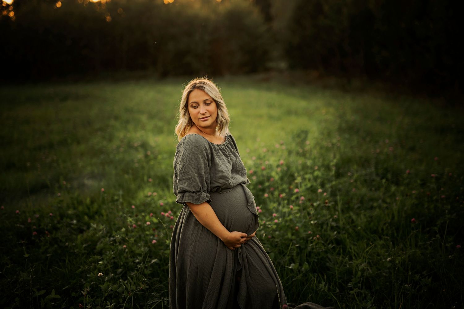 Peaceful maternity photo in natural setting with warm sunset lighting.