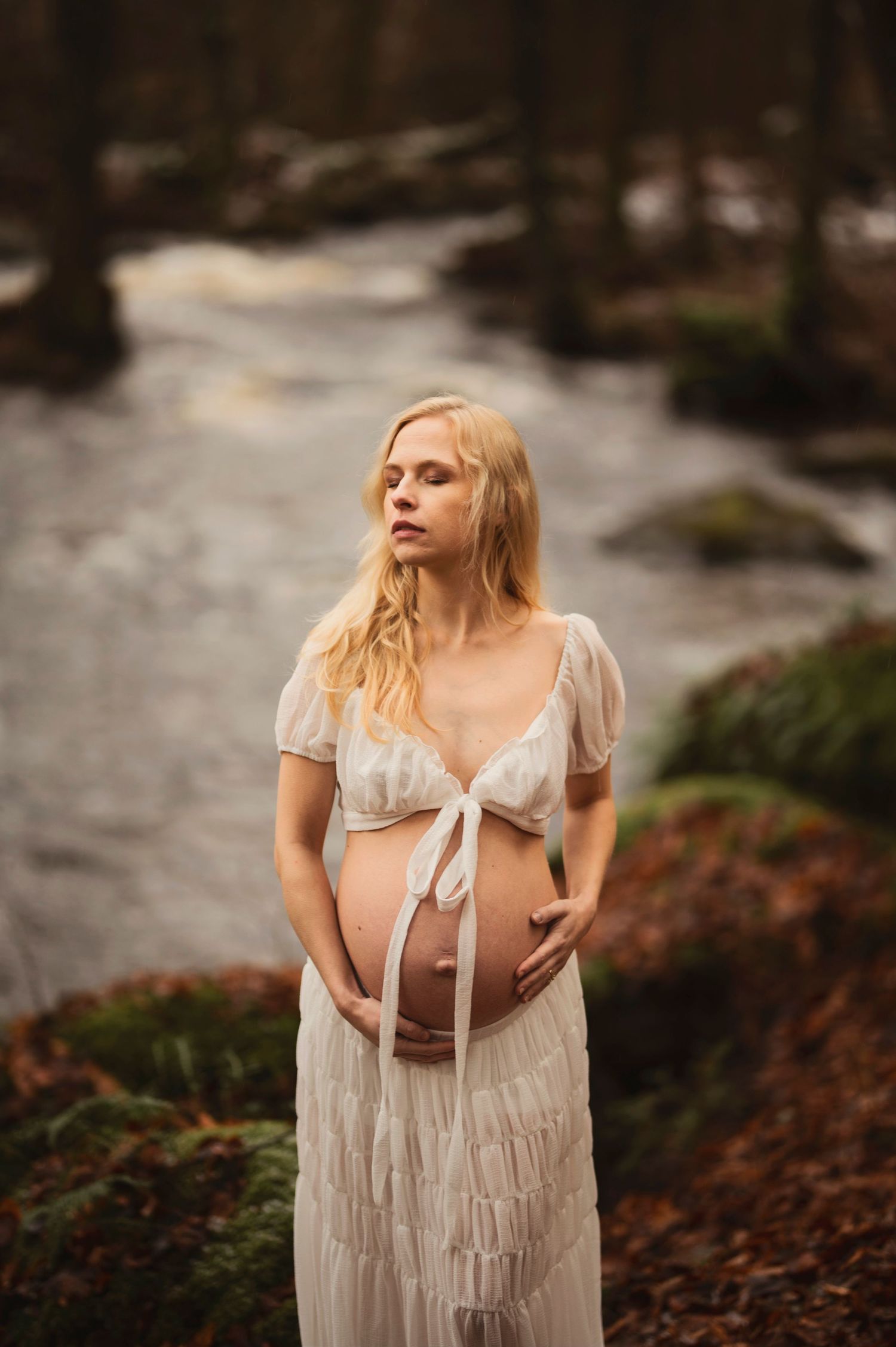 Vacker gravid kvinna på fotografering vid en bäck. Fotograf är Lovestories By Sara.