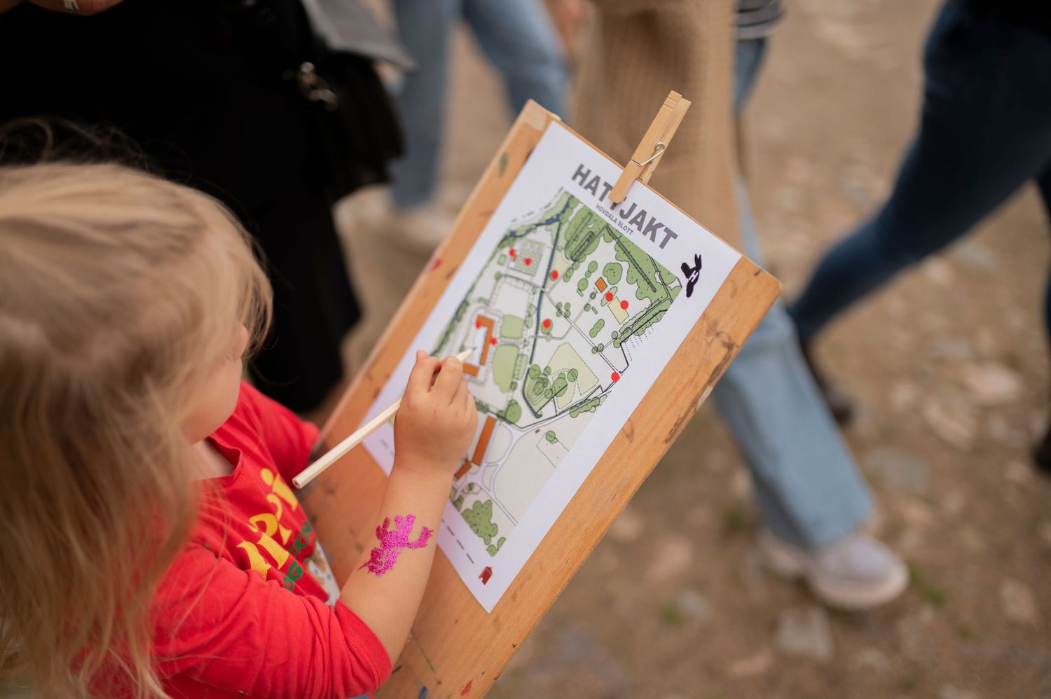 Child points to illustrated map on wooden display board during outdoor activity.