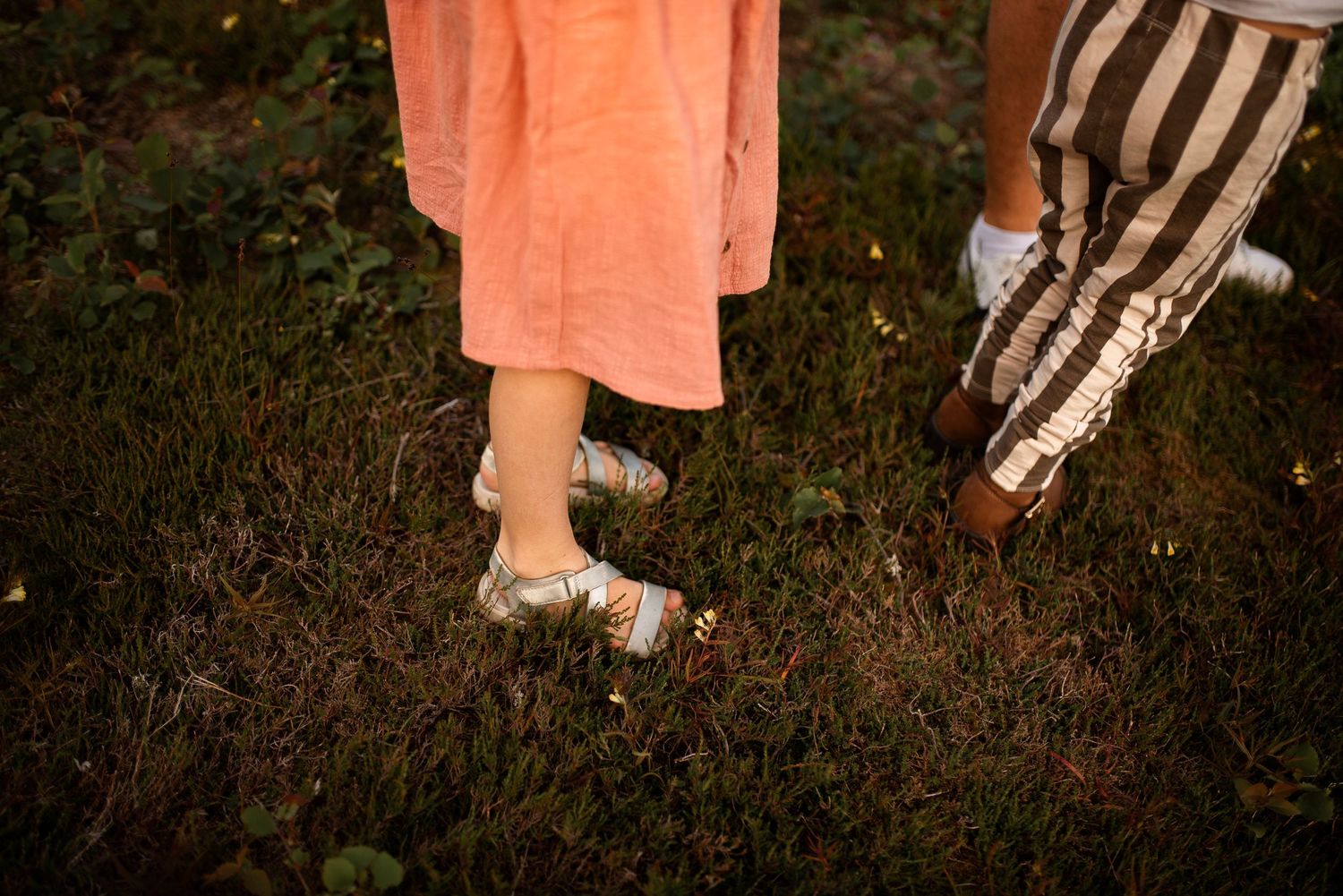 Close-up view of feet in summer shoes walking on grass at sunset.