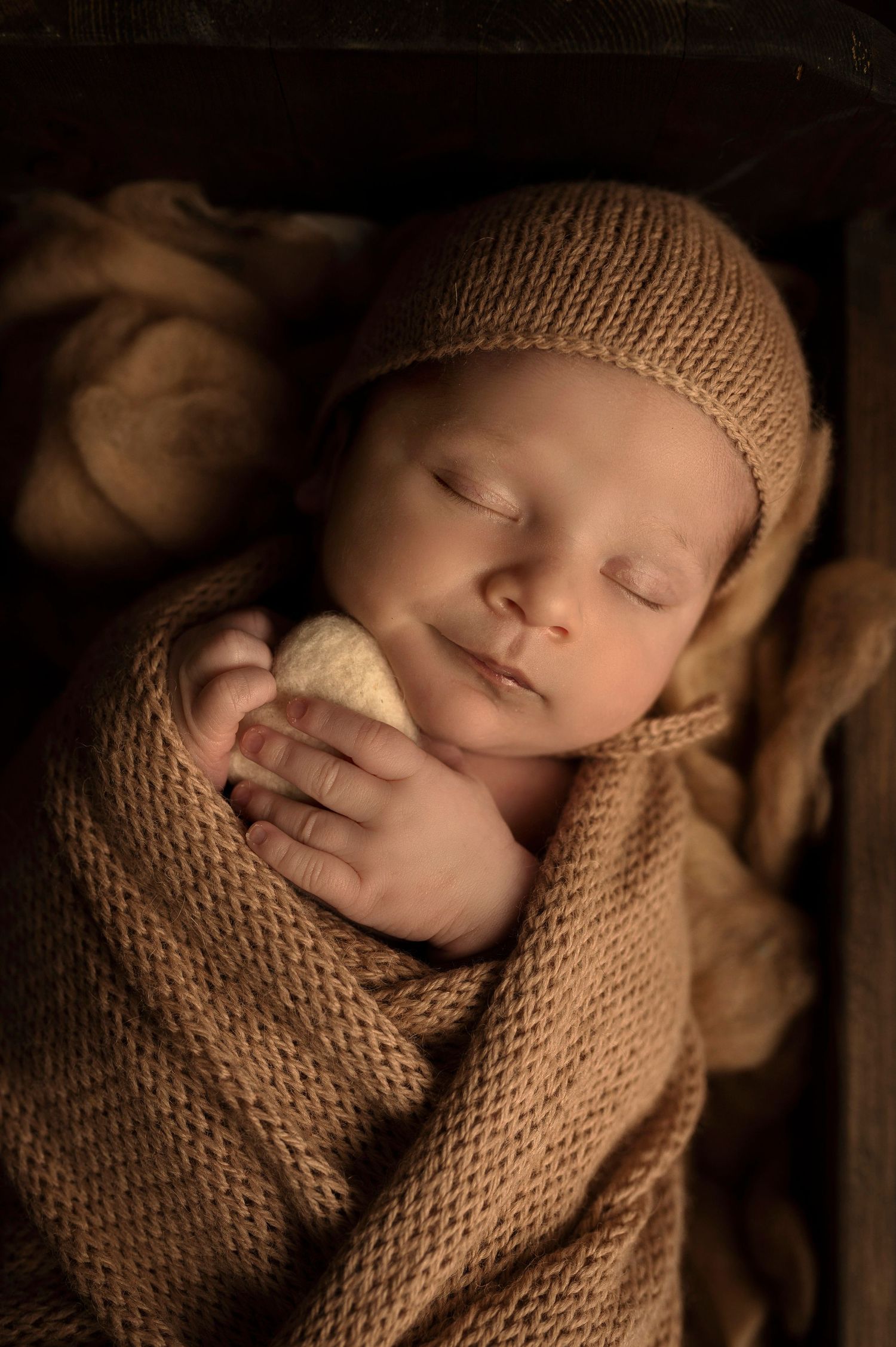 Peaceful newborn in brown knit wrap and hat sleeping.