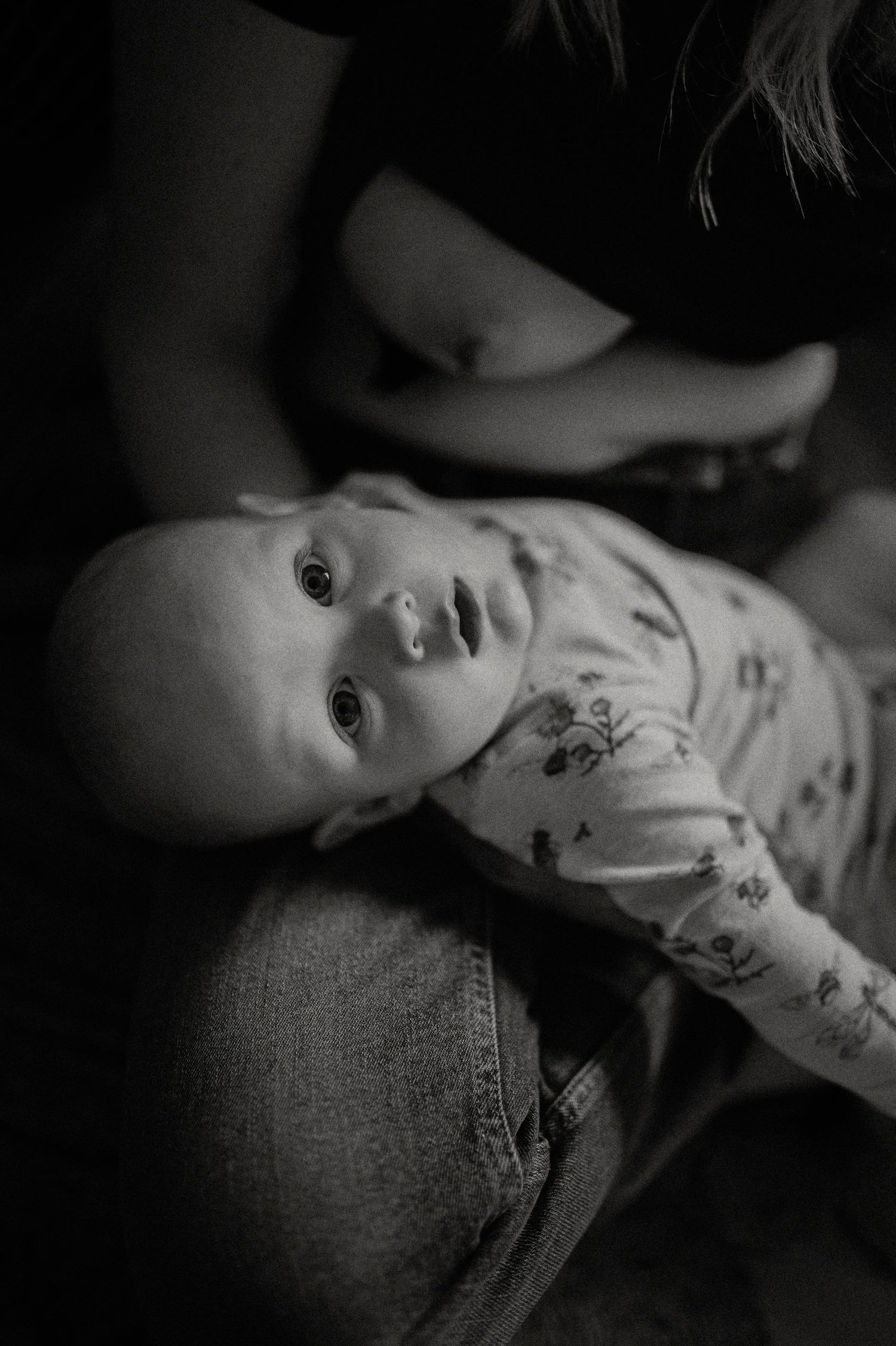 Black and white portrait of an infant lying on their back with curious expression.