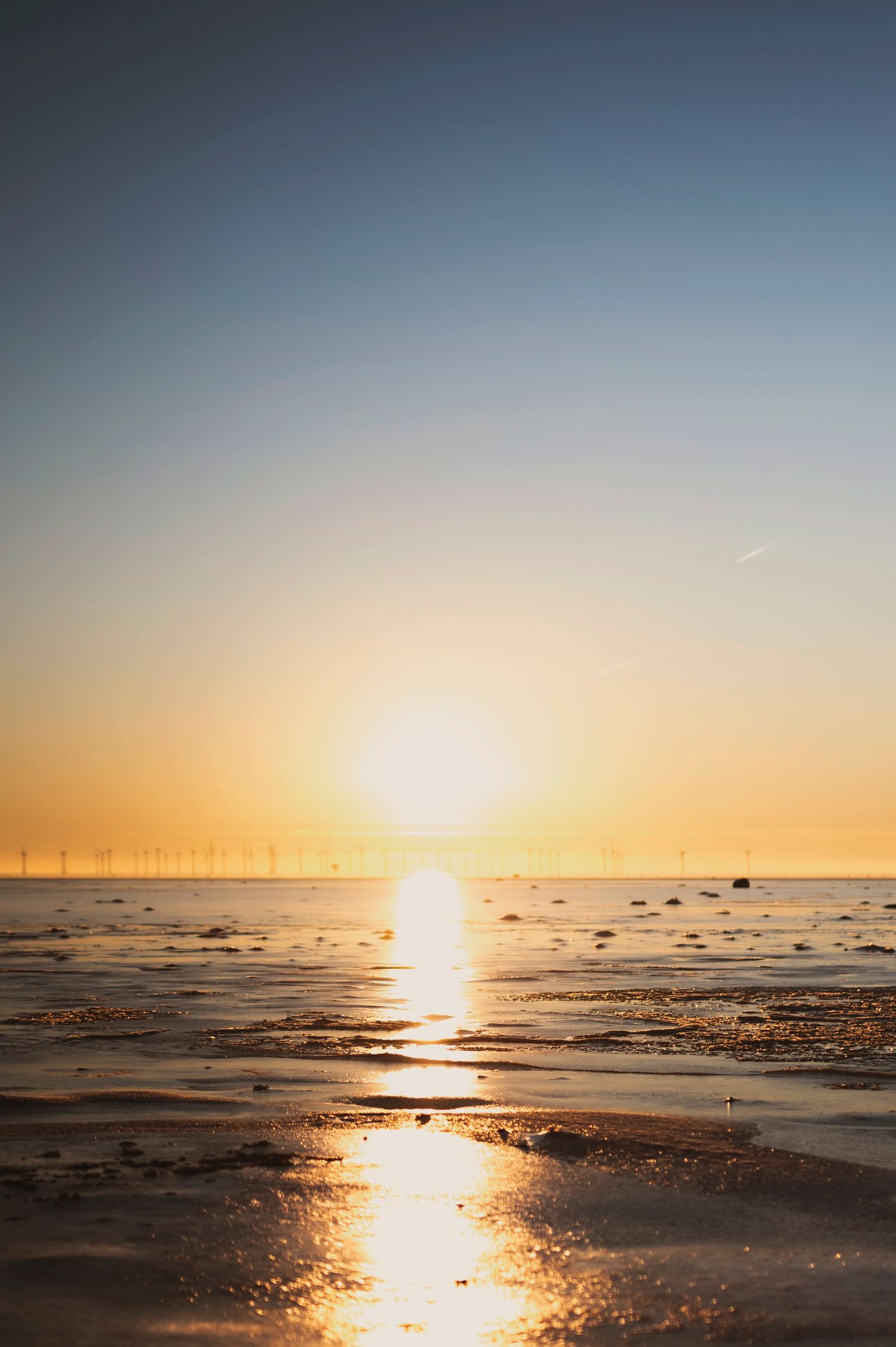 Beautiful sunset over calm ocean waters with wind turbines visible on the horizon.