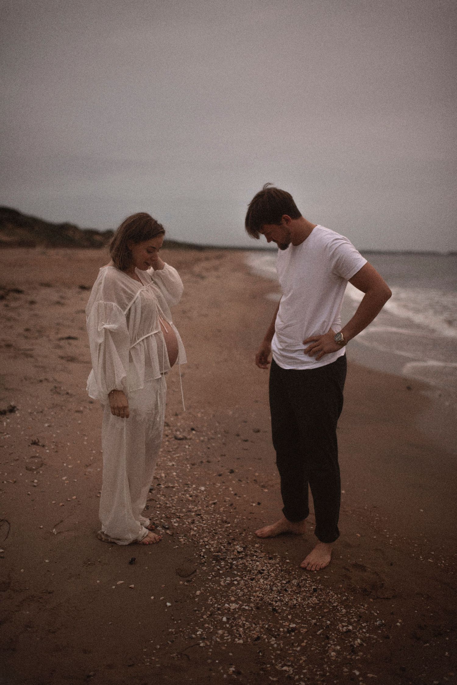 Couple in casual attire shares conversation while standing on beach at dusk.