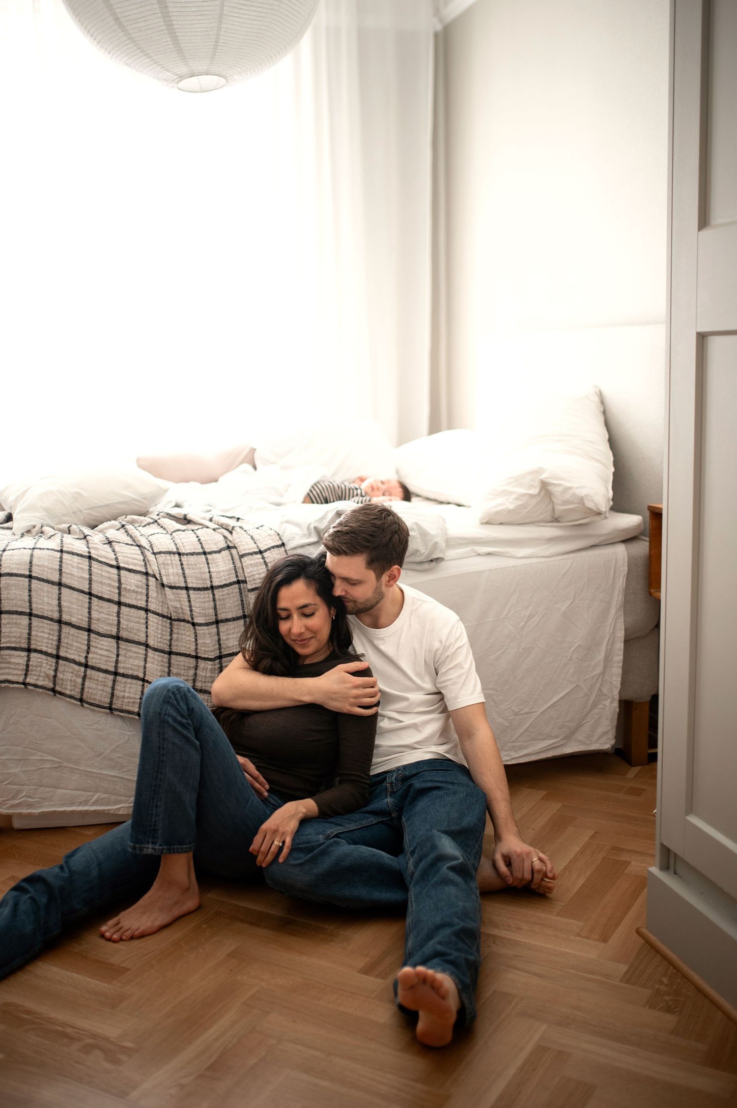 A loving couple sits on the floor leaning against a bed in a cozy bedroom.