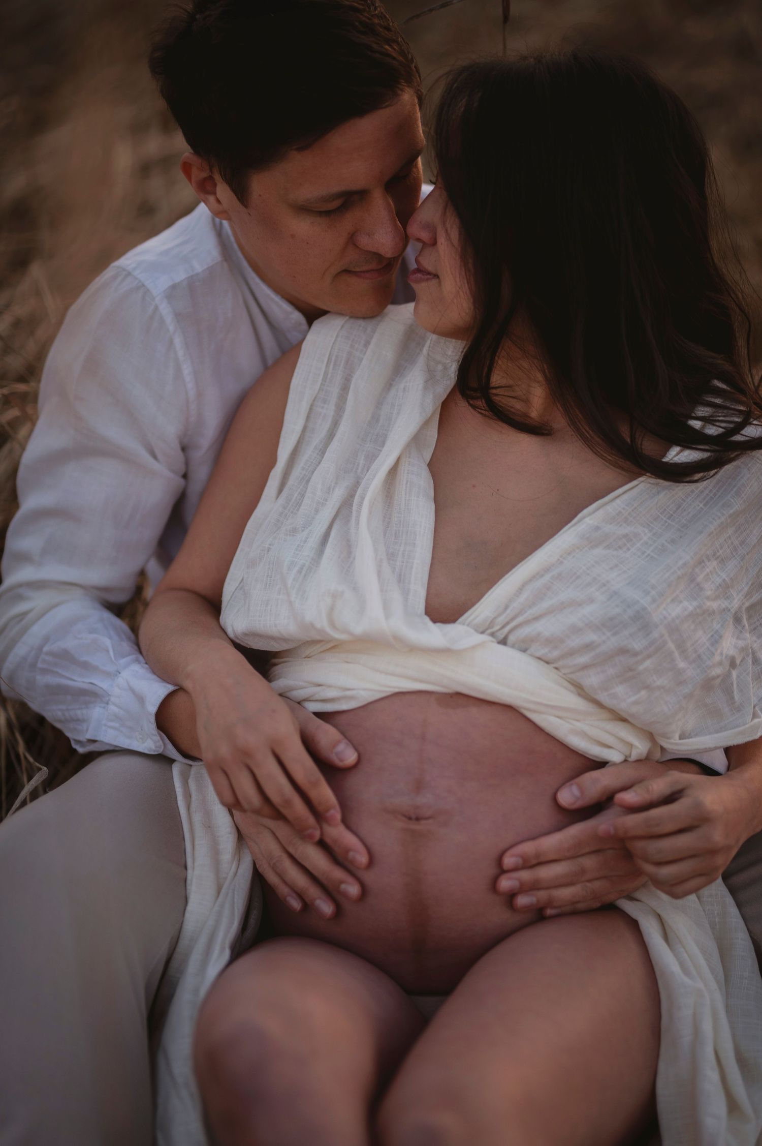 An intimate maternity photo showing a couple in white clothing embracing while highlighting the pregnant belly.