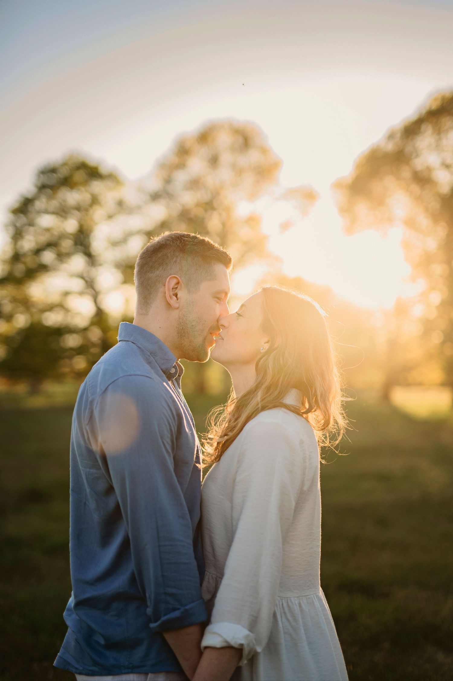Romantic couple sharing intimate moment at sunset in park with trees silhouetted in background.