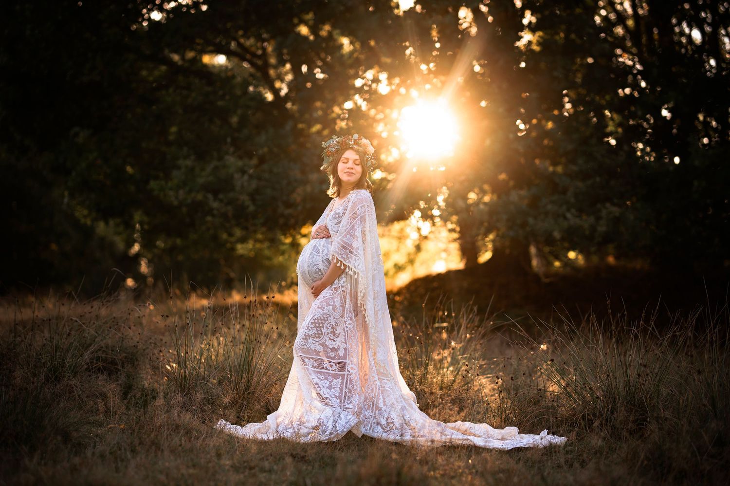 Dreamy maternity portrait in white lace dress with sun flare in rustic field setting.