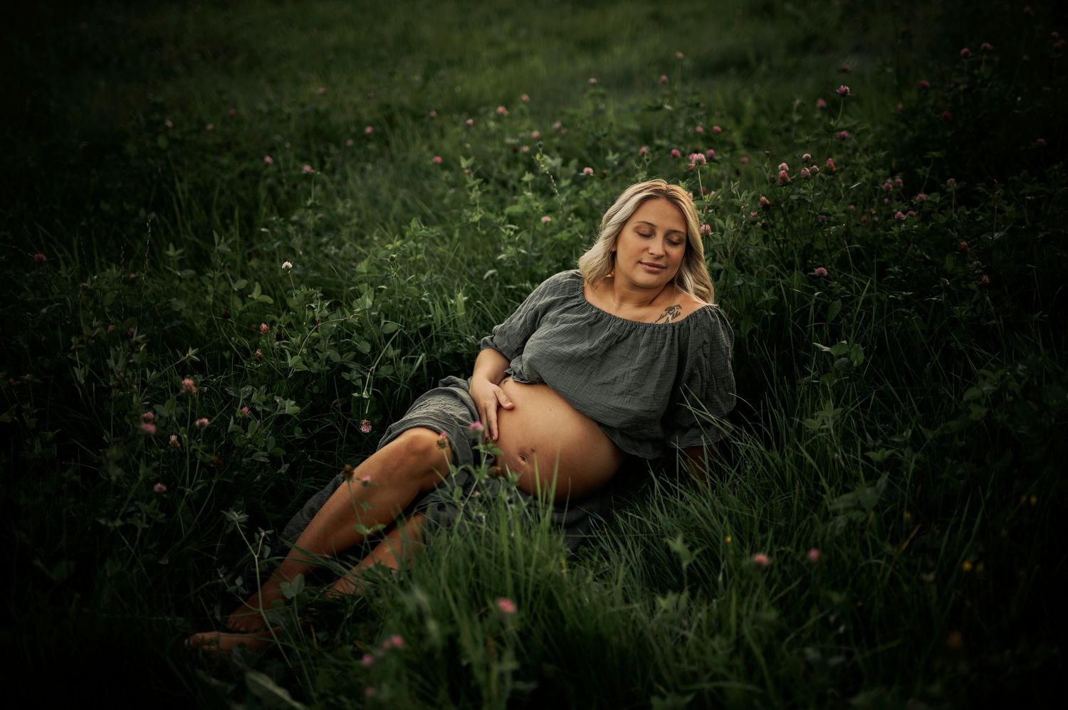 Relaxed maternity portrait in rustic outdoor setting with brown boots and gray dress.