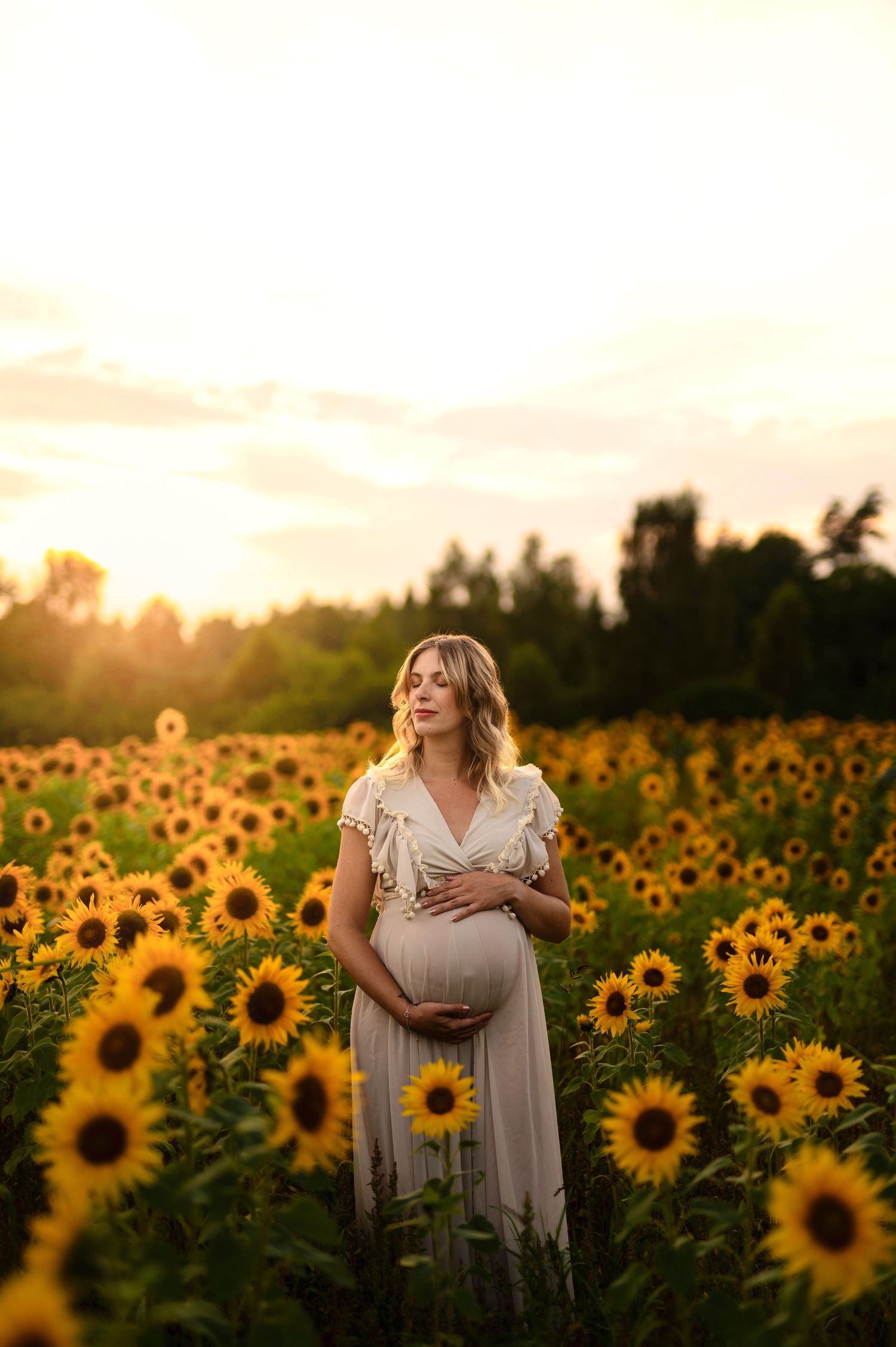 Ethereal maternity moment captured in sunflower field during sunset.