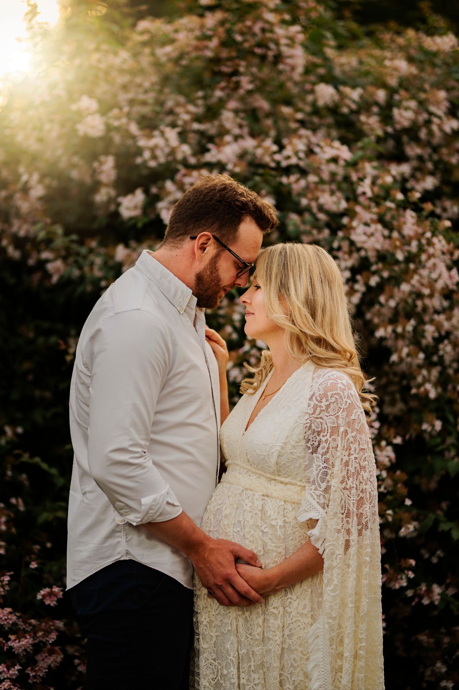 Romantic sunset maternity photo with couple in white lace dress and casual attire.