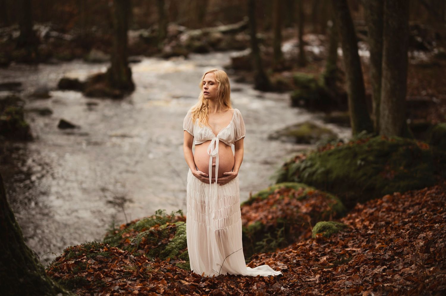 Vacker gravid kvinna på fotografering vid en bäck. Fotograf är Lovestories By Sara.