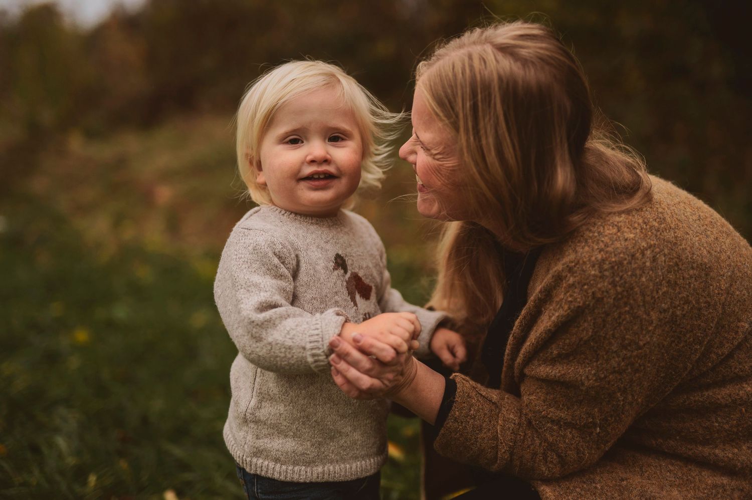 Intimate outdoor moment captured against autumn foliage wearing matching grey and brown sweaters.