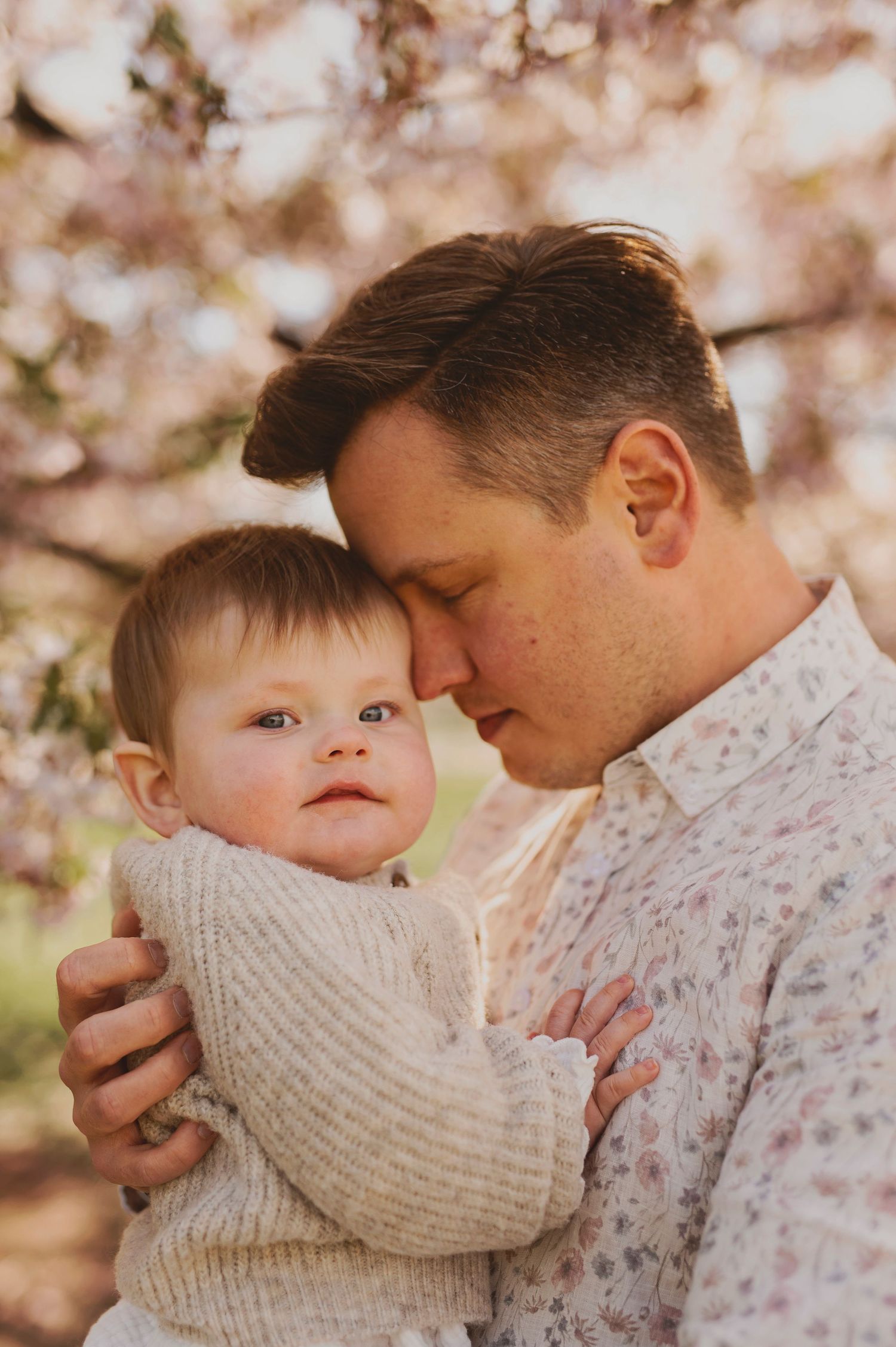 A tender moment between parent and baby under flowering spring trees.