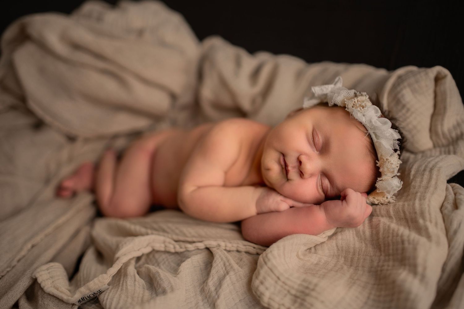 Sleeping baby in vintage-style lace bonnet laying on cream colored textured blanket.
