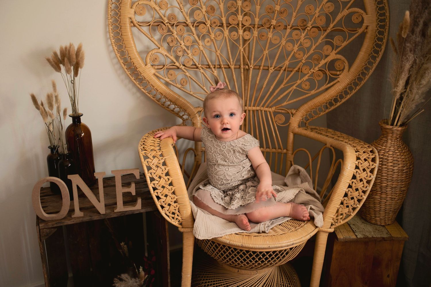 A decorative photo setup featuring a baby in a wicker peacock chair with boho accents.
