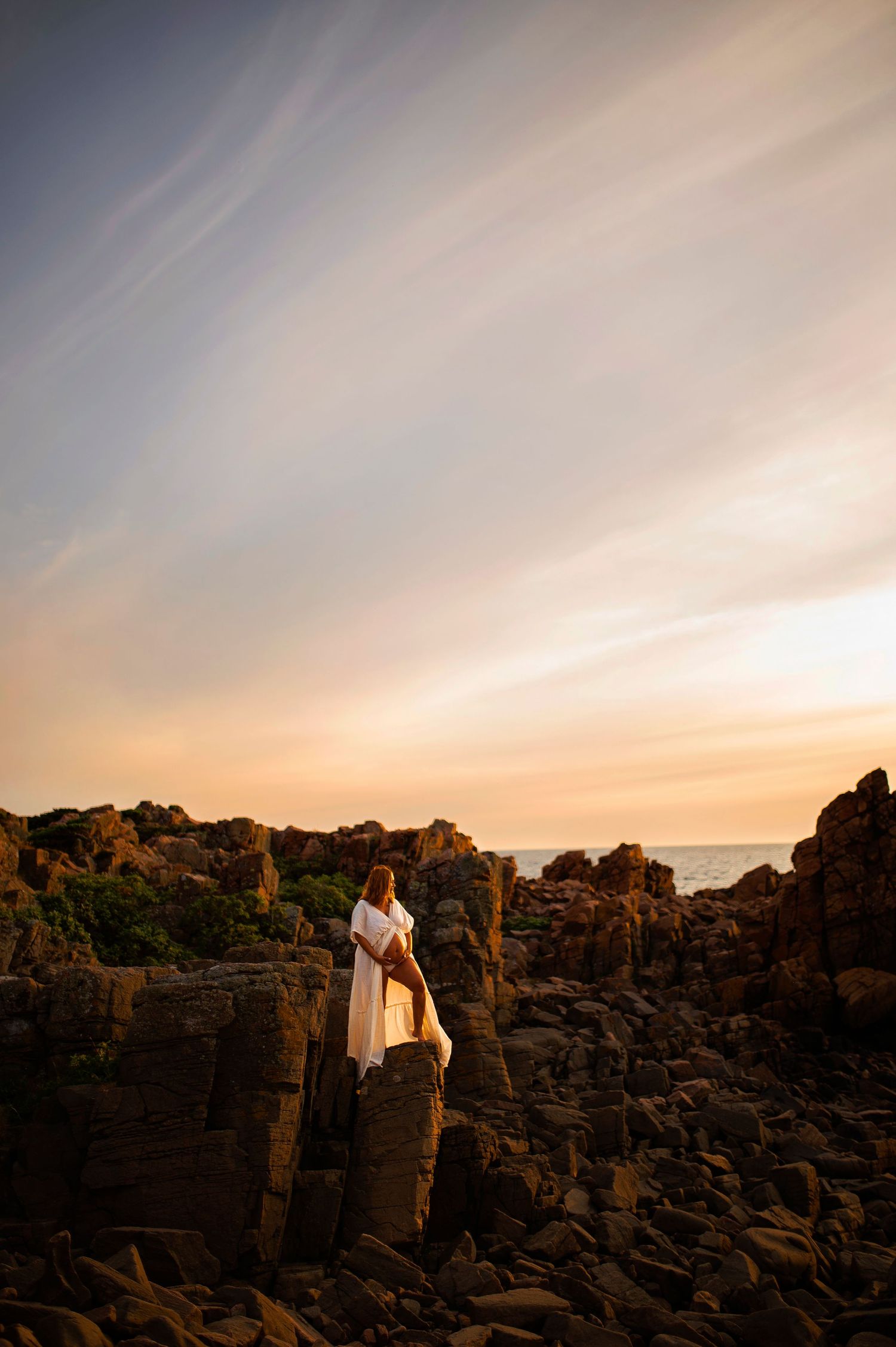 Silhouette of figures standing on dramatic rocky coastline during golden sunset.