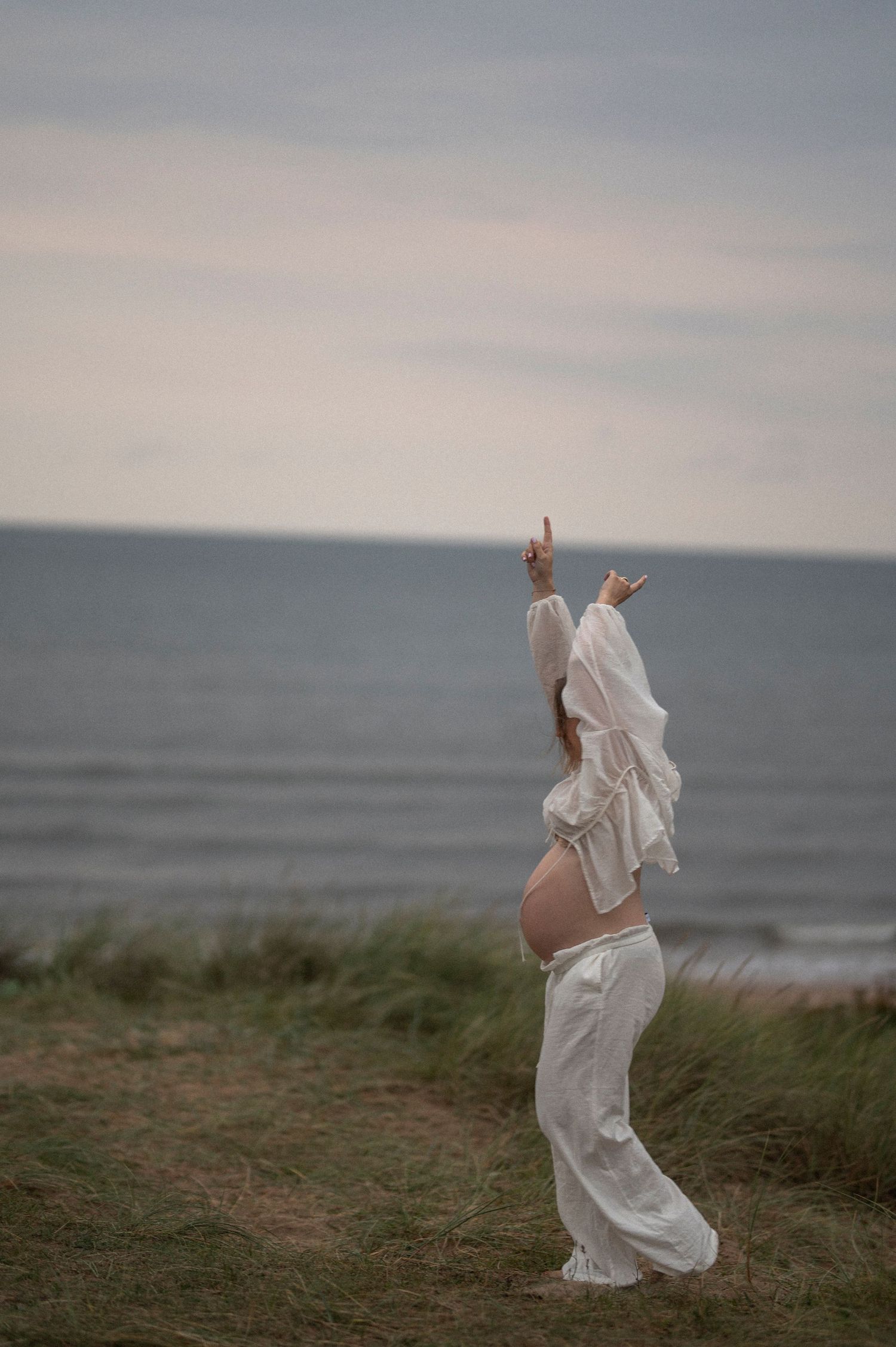 A dancing figure in white raises their arms triumphantly against an ocean backdrop.