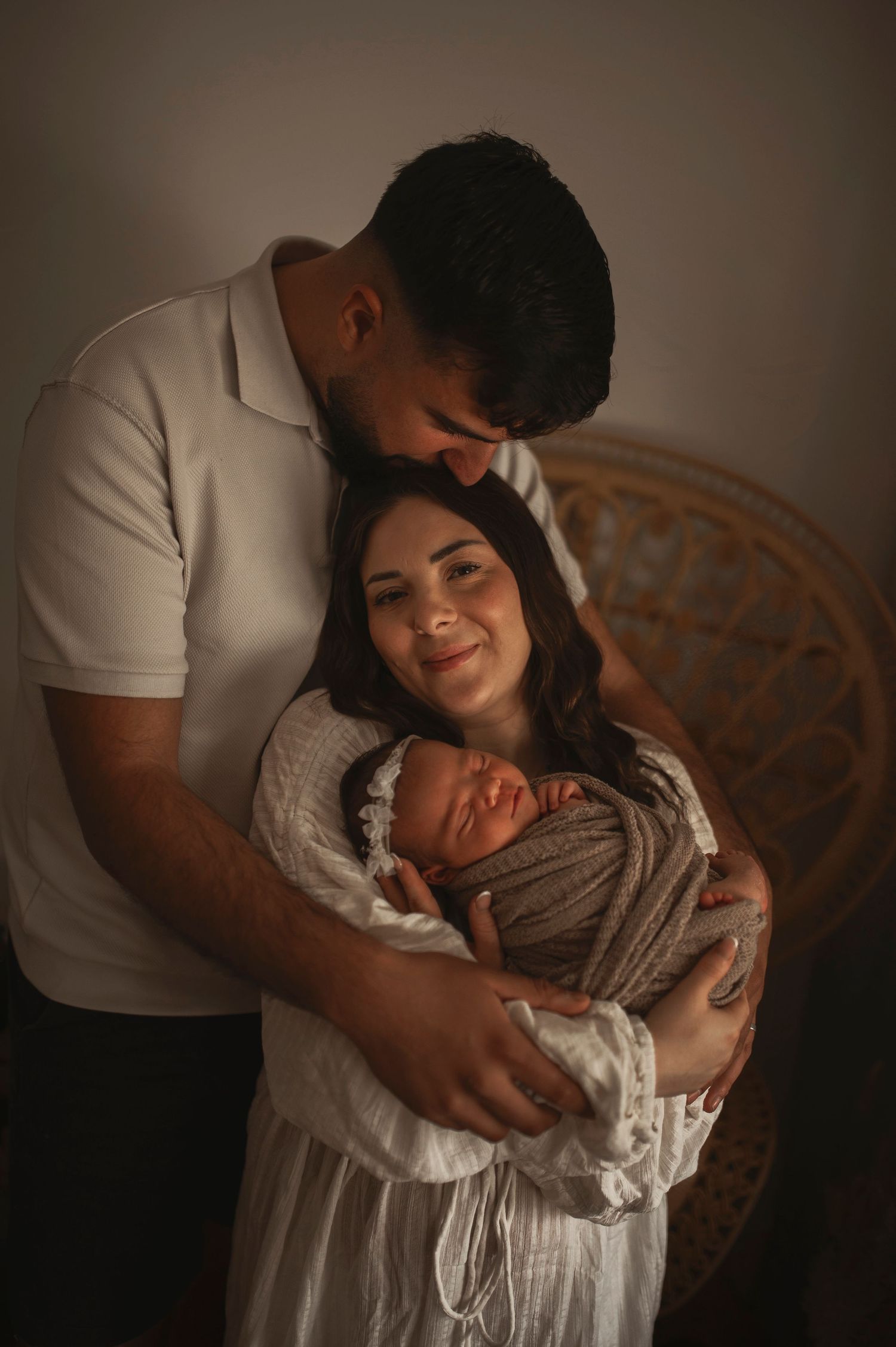 A tender family moment captured in warm lighting as parents cradle their newborn baby in a cozy indoor setting.