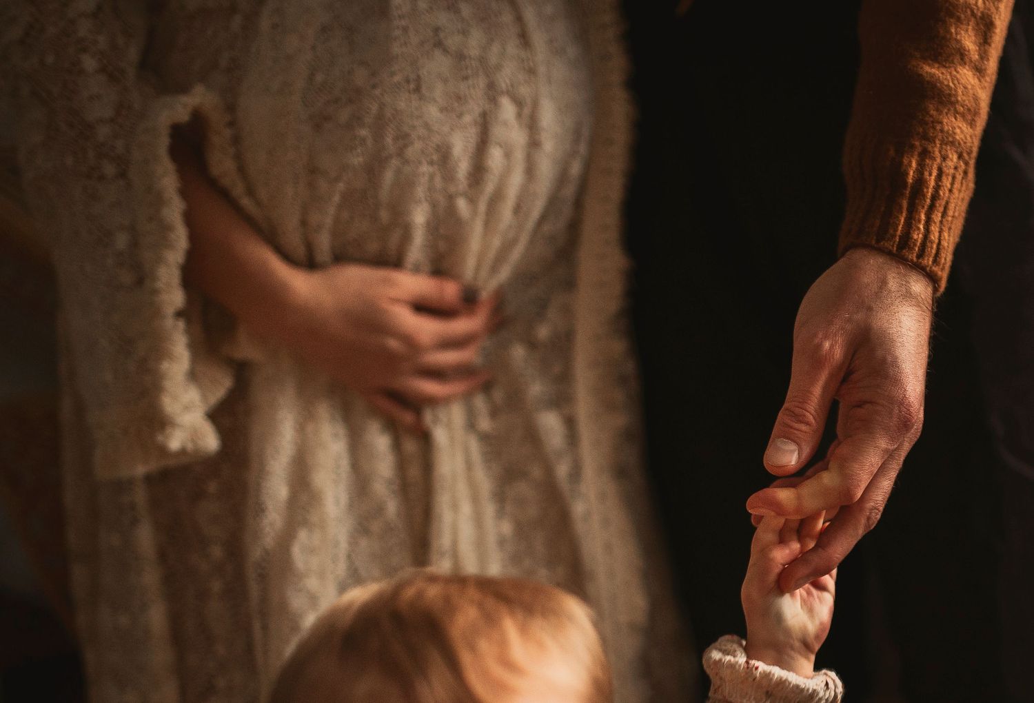 Close-up shot of hands tenderly touching in warm light against lace fabric and earthy tones.