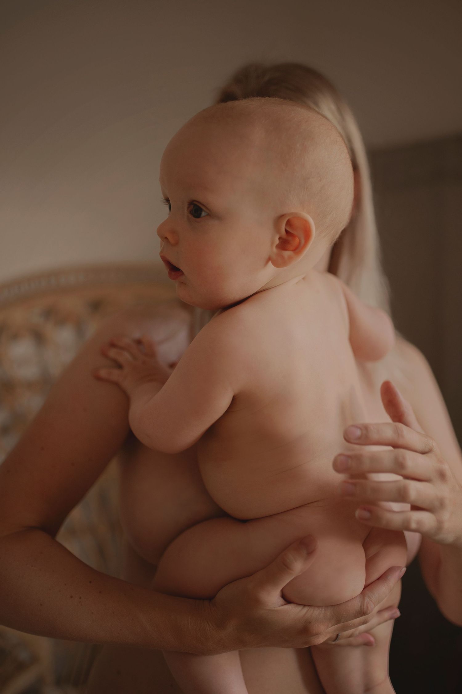 Side view of baby being held against neutral background in natural lighting.