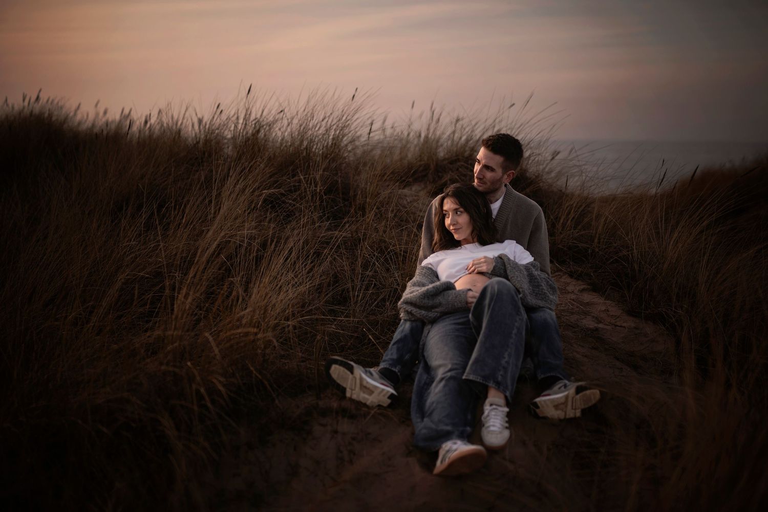 Couple embracing on grassy hillside during sunset.