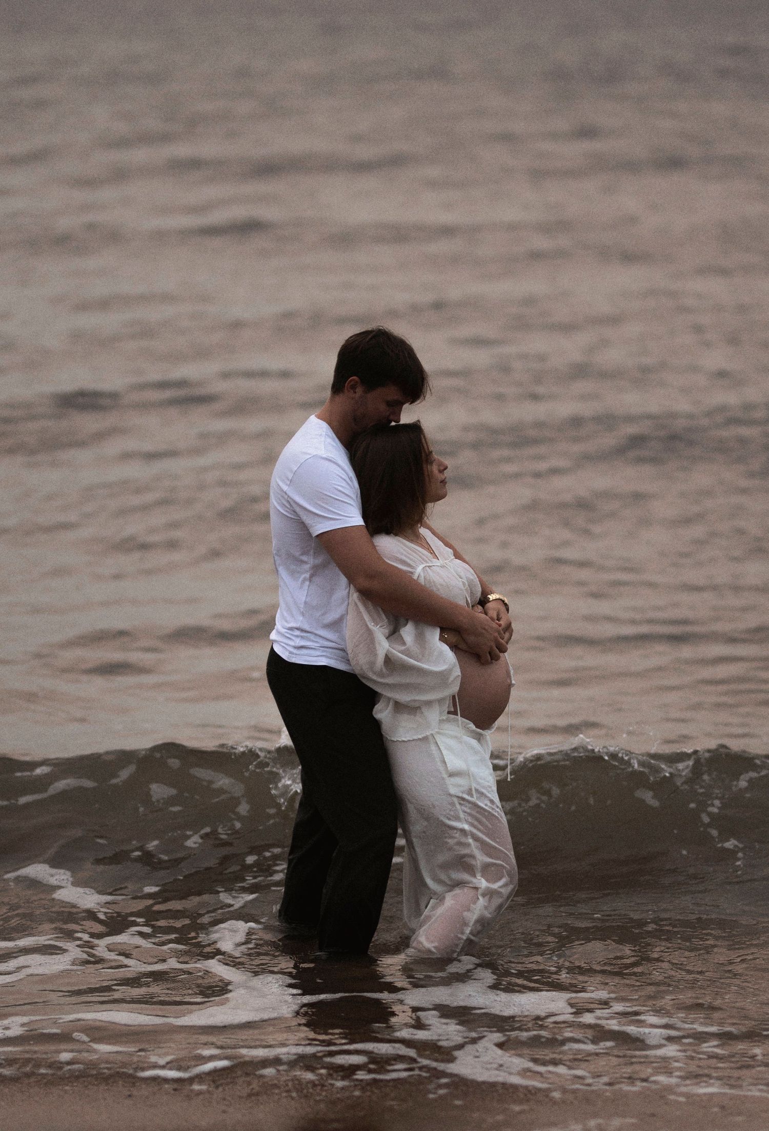 A couple embraces while standing in ocean waves during a romantic beach photoshoot.
