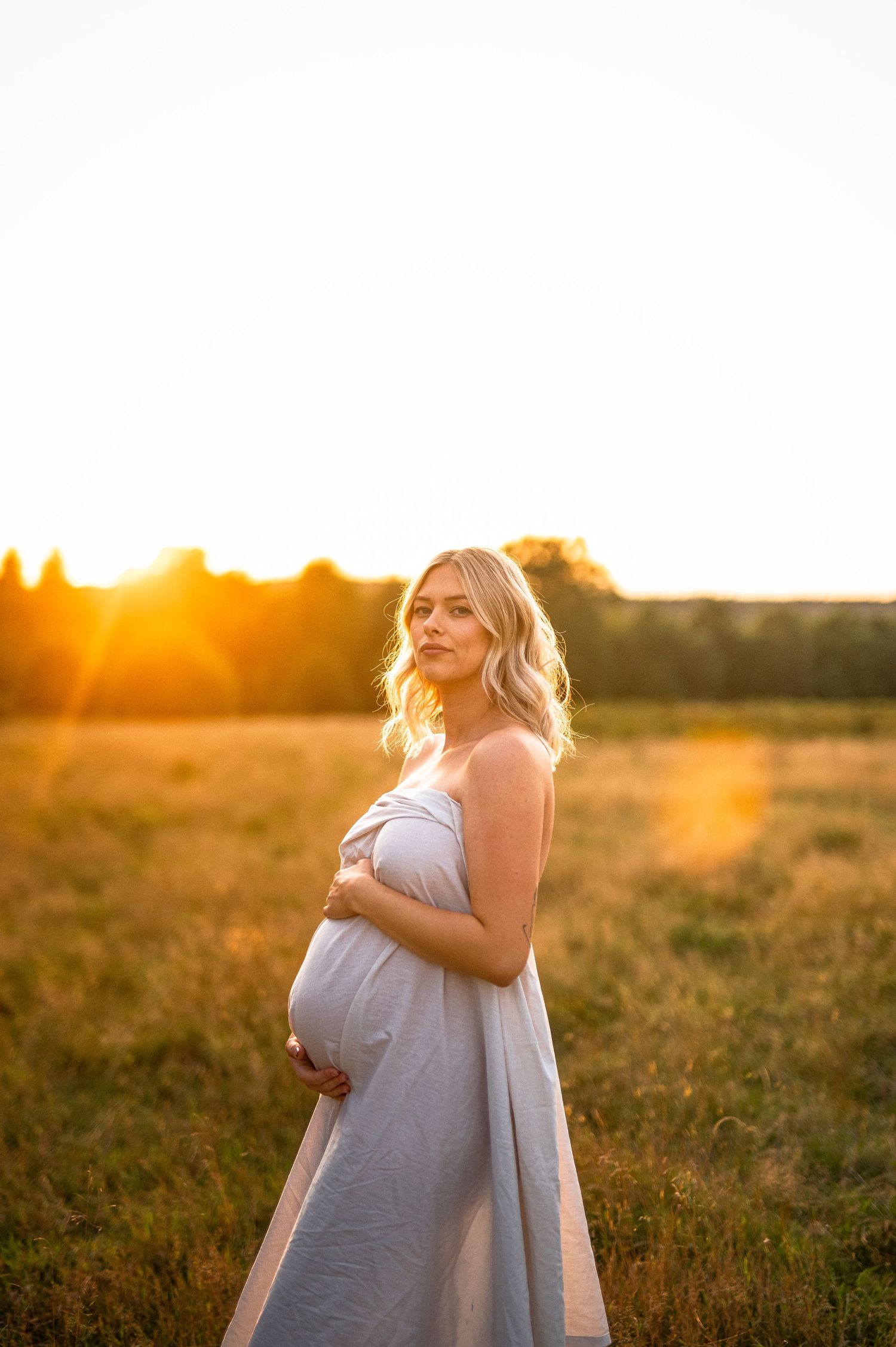 Serene maternity portrait in simple dress during golden hour in summer field.