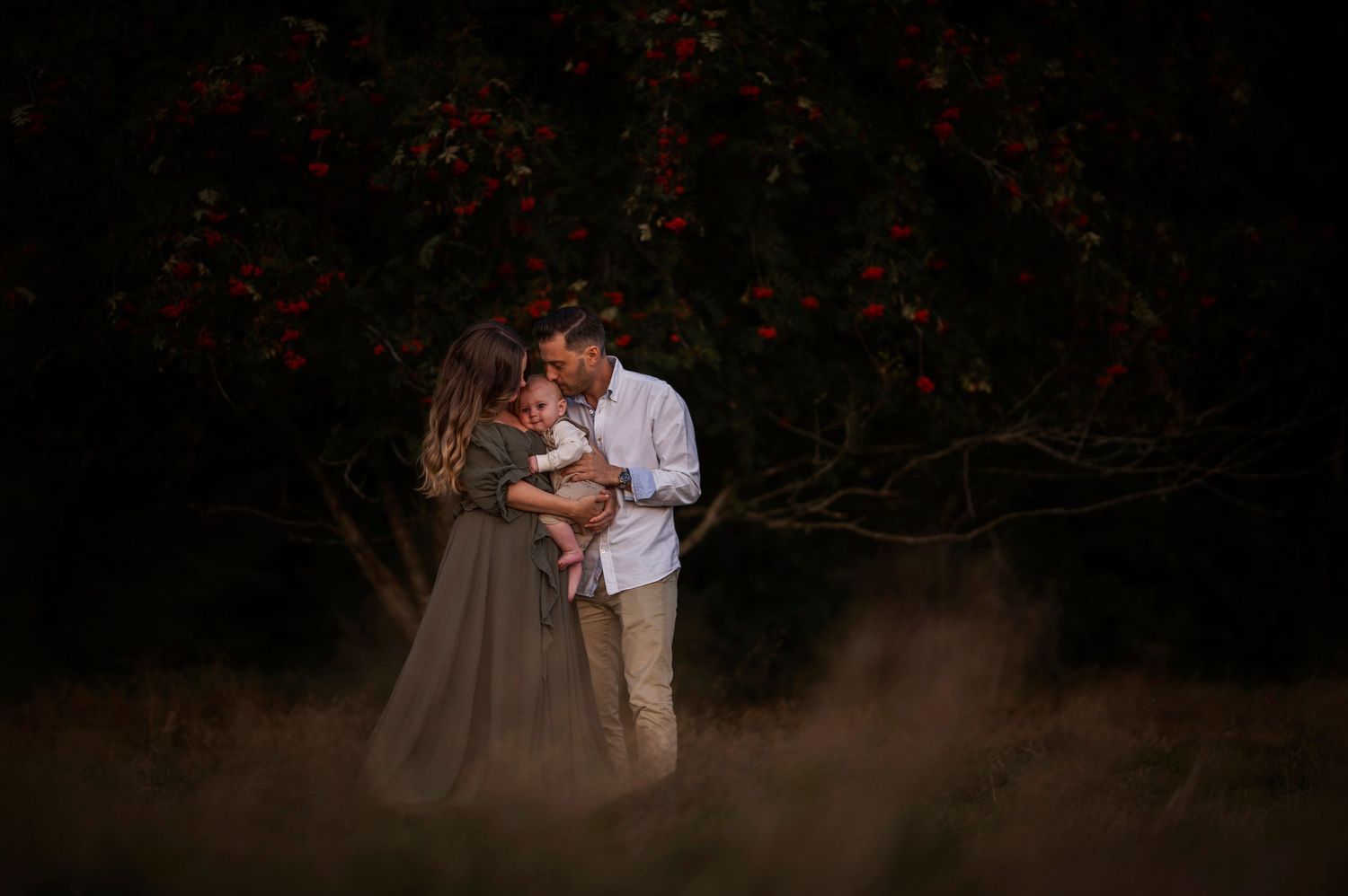 A romantic couple embraces in front of blooming red flowers at dusk creating a moody atmosphere.
