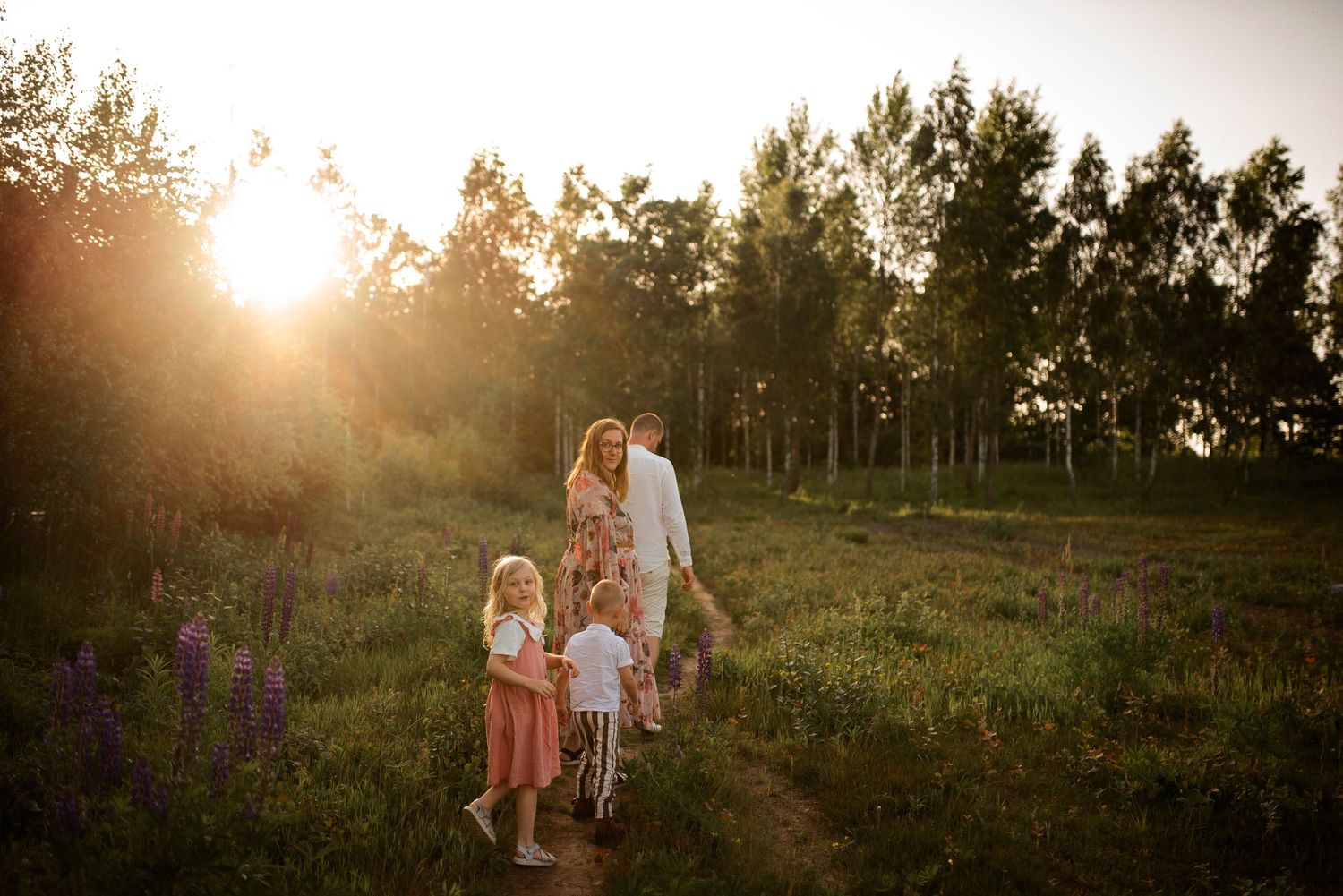 Family walking through a meadow with purple wildflowers at sunset.