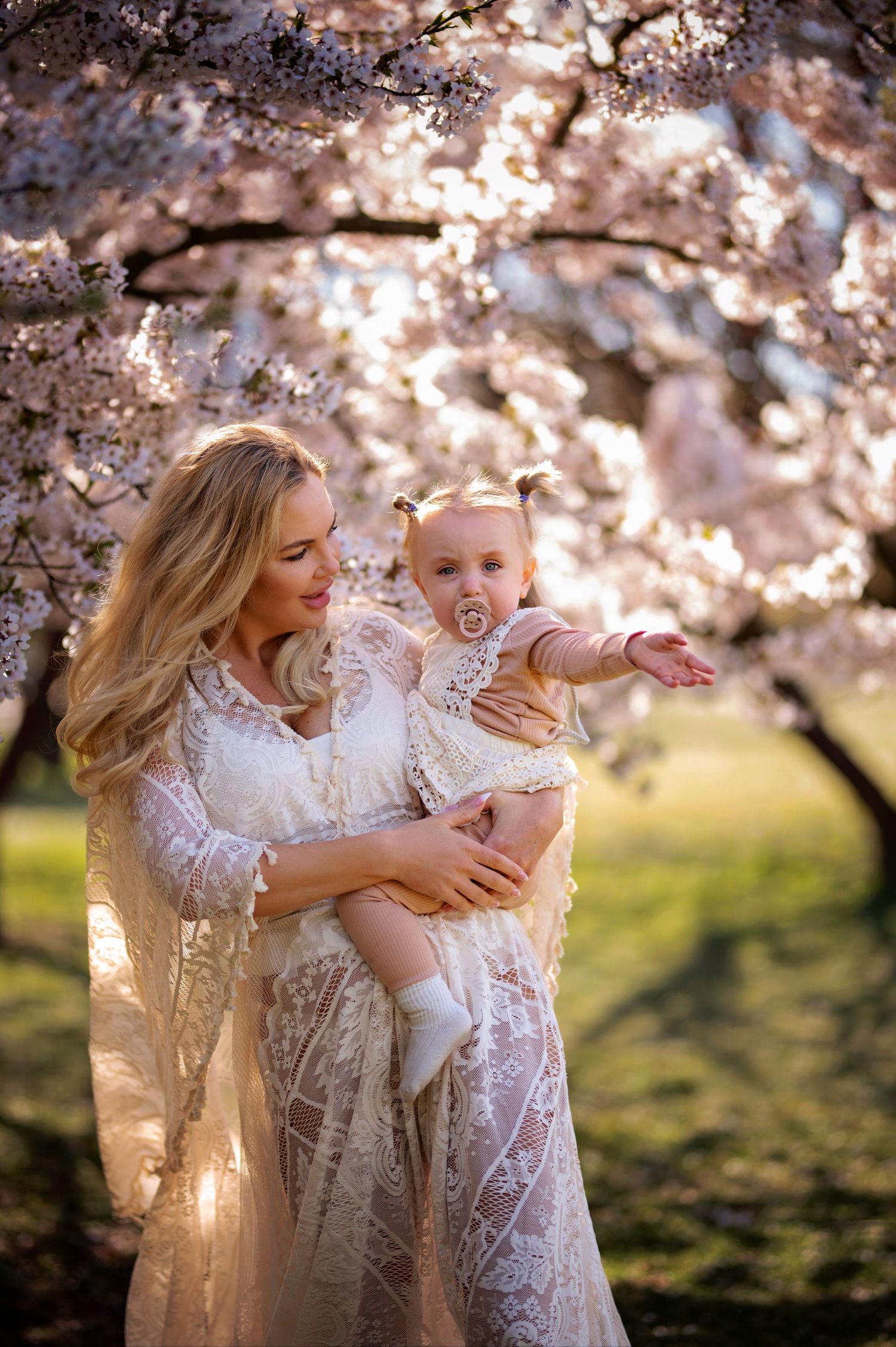 A magical spring photo under blooming cherry blossoms featuring whimsical white lace dresses and joyful expressions.