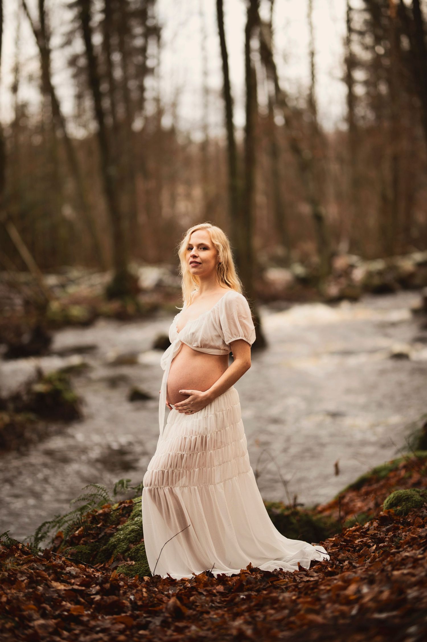 Vacker gravid kvinna på fotografering vid en bäck. Fotograf är Lovestories By Sara.