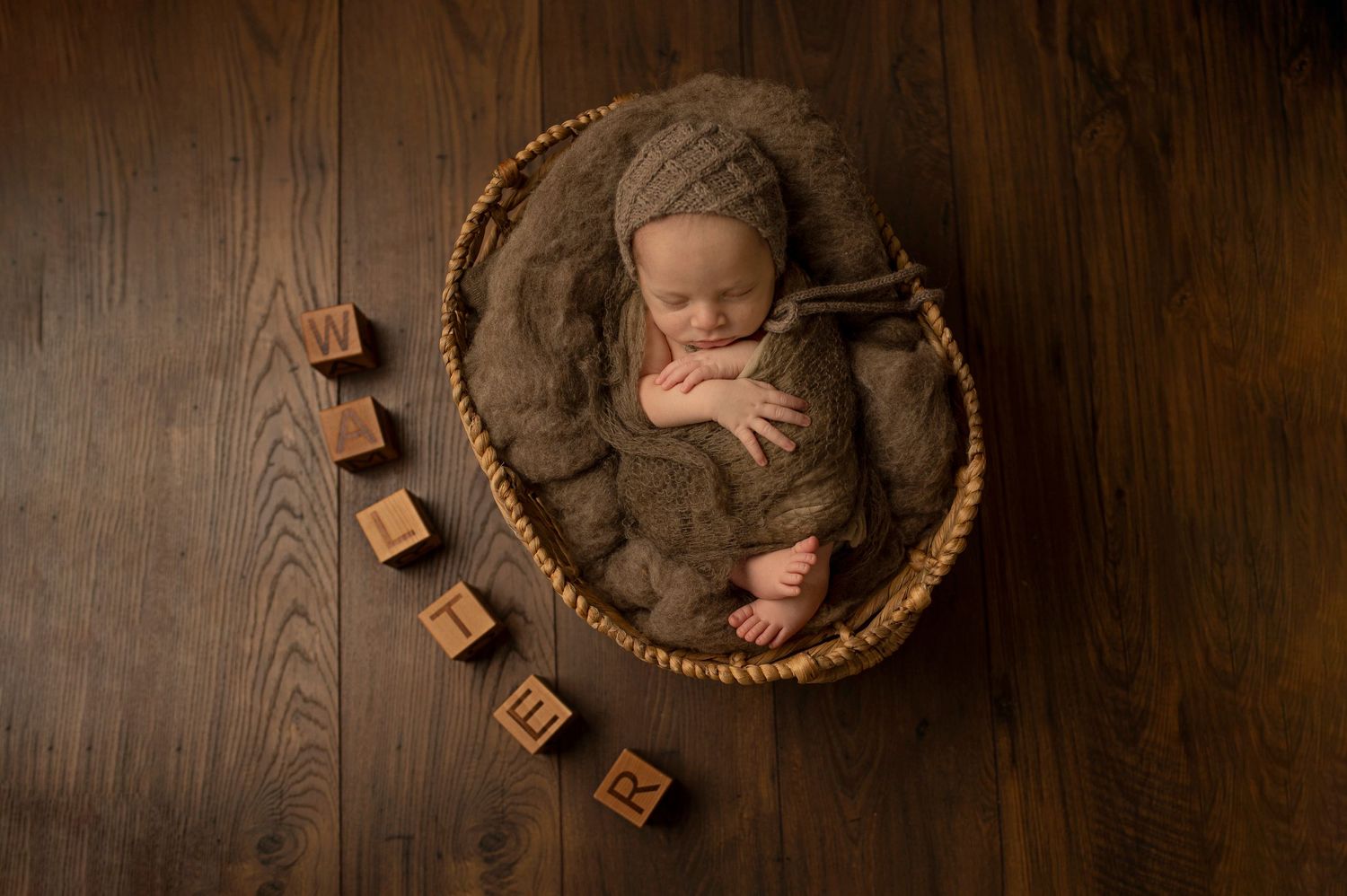 Sleeping baby in round basket with wooden blocks on hardwood floor.