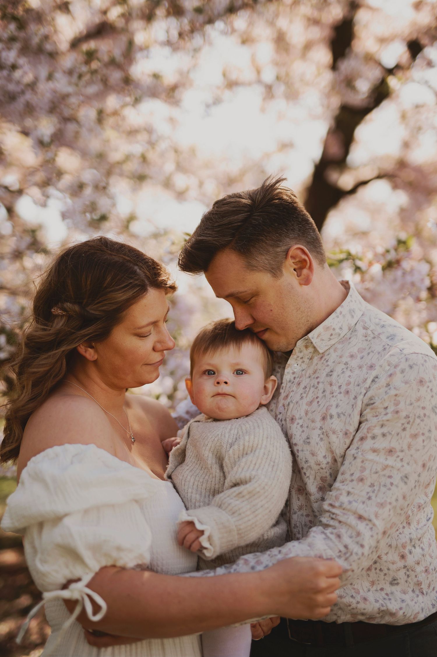 A family shares an intimate moment together beneath pink cherry blossom trees.