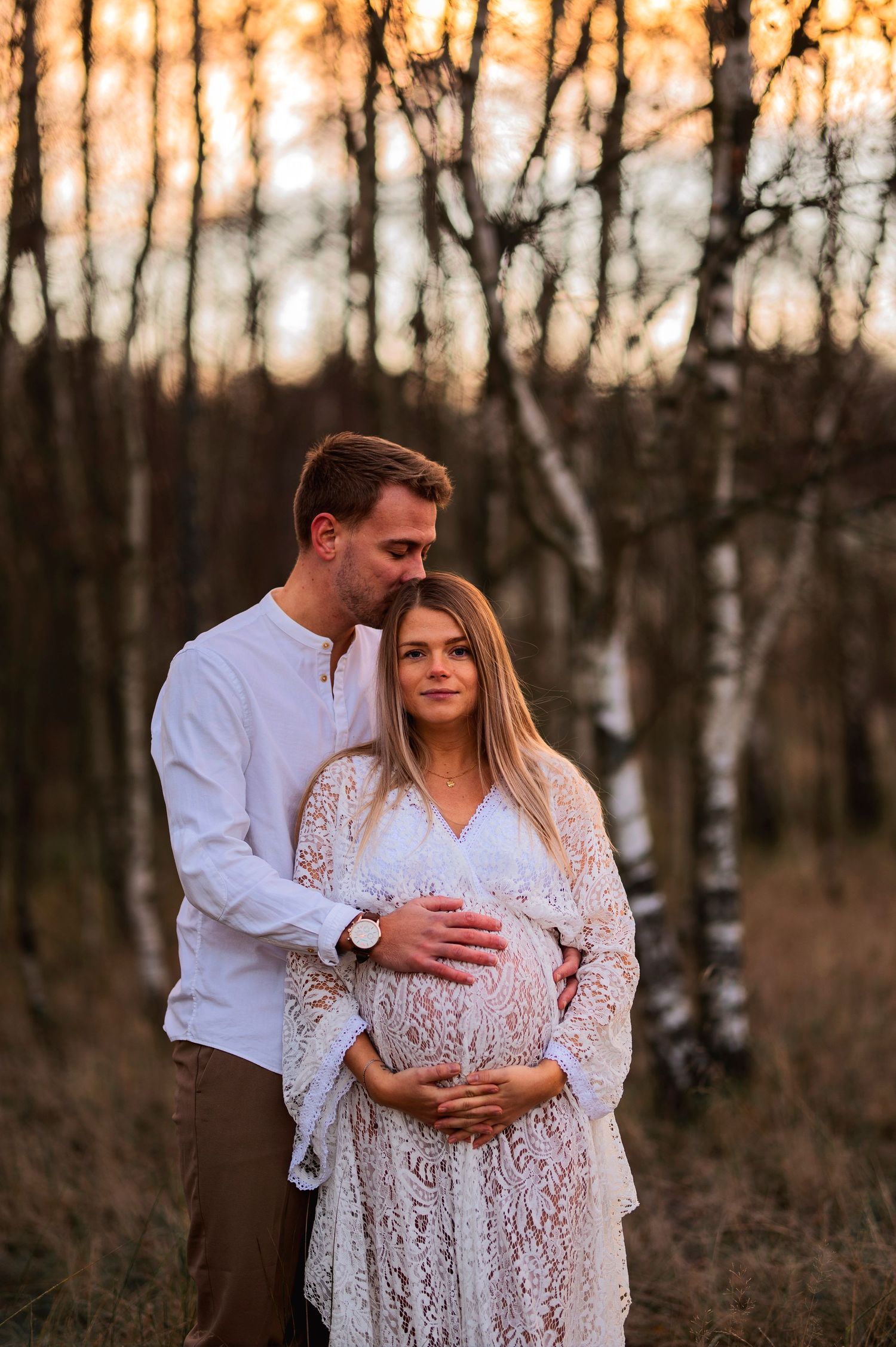 Couple embracing in birch forest during golden hour.