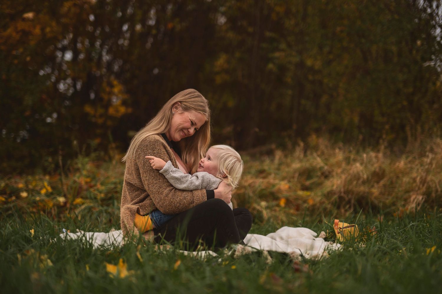 Intimate nursing session photographed in a field with fall foliage.