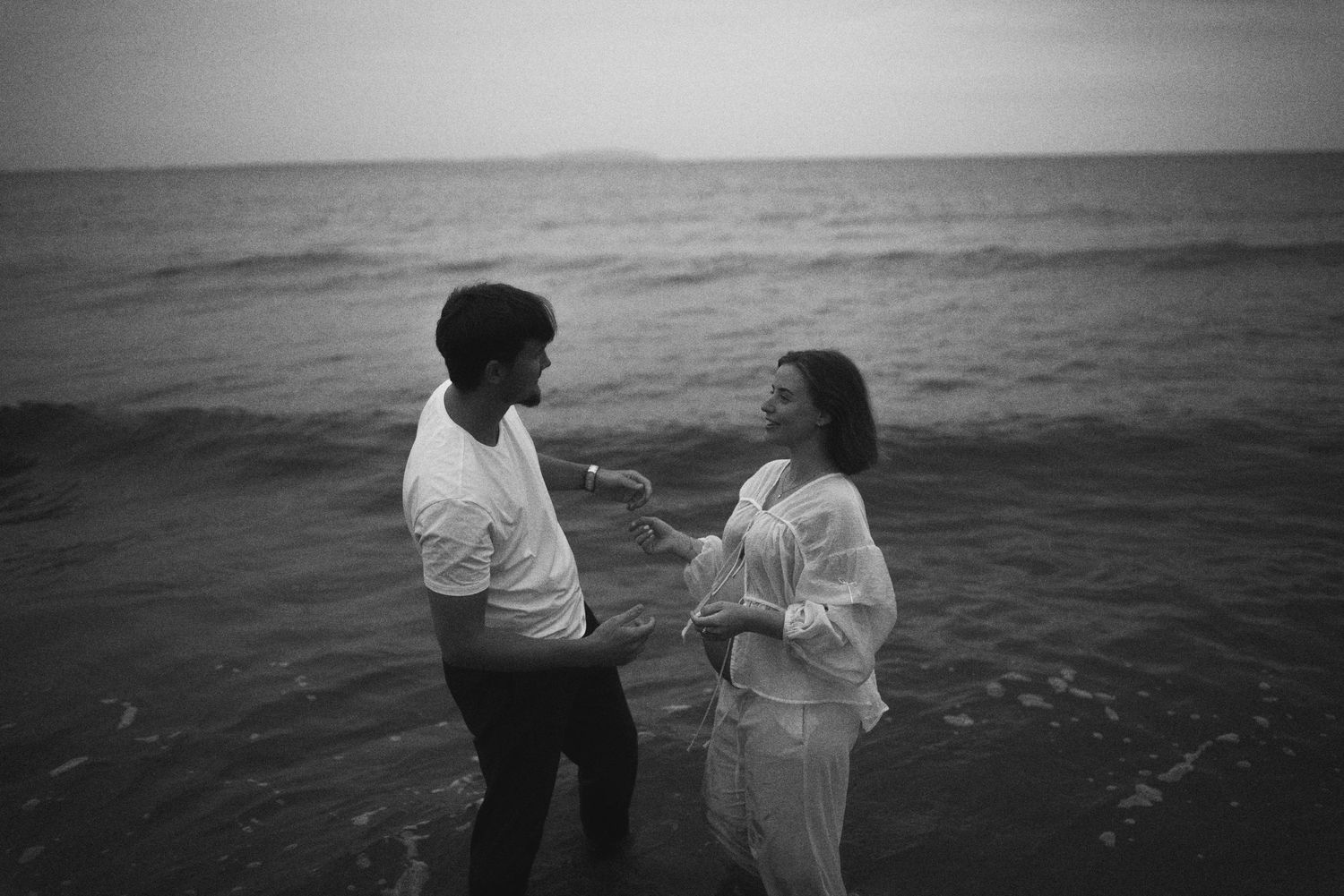 A black and white capture of a couple sharing an intimate moment by the ocean.