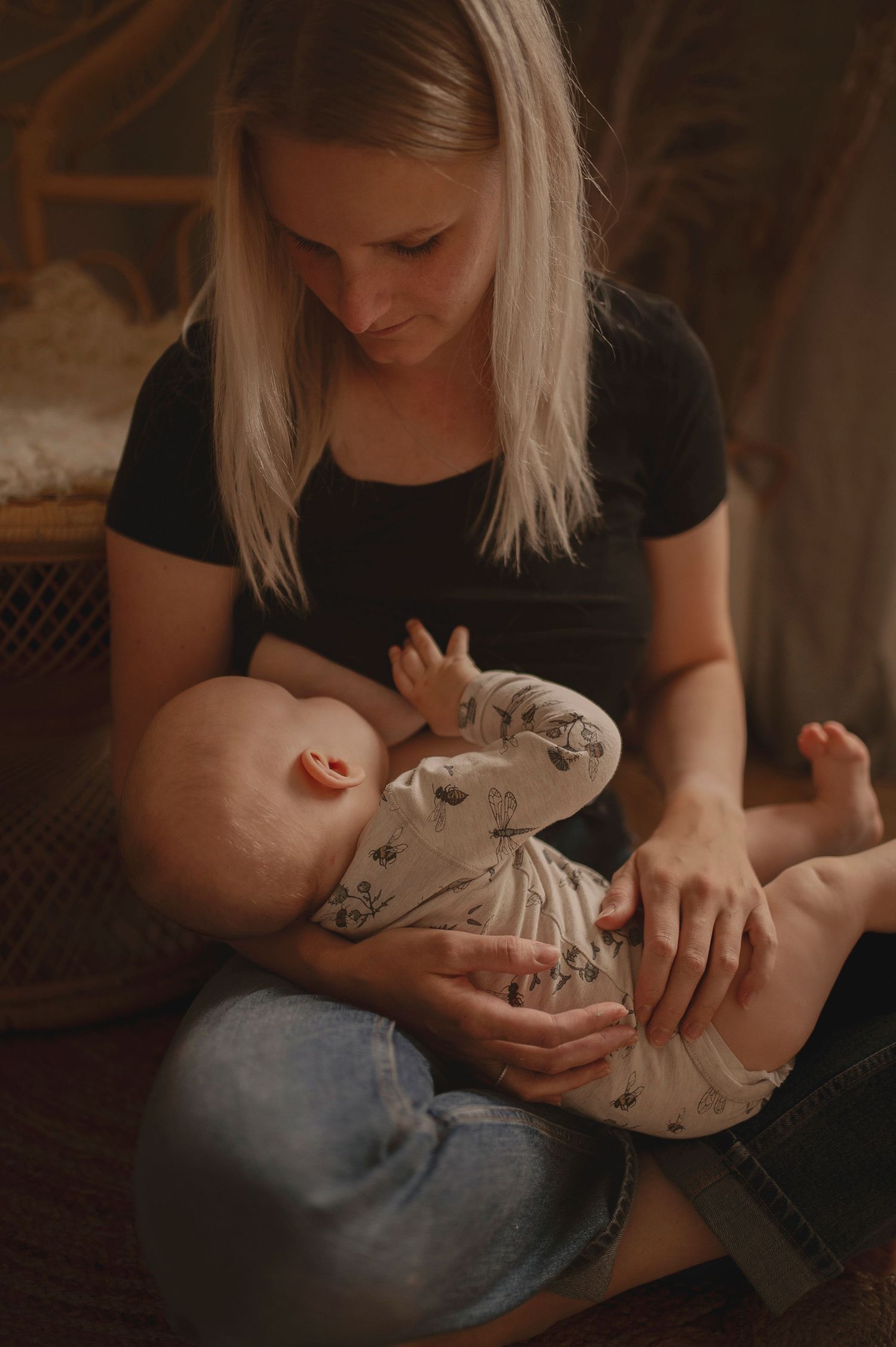 Intimate nurturing moment captured in warm tones with a decorative rattan chair backdrop.