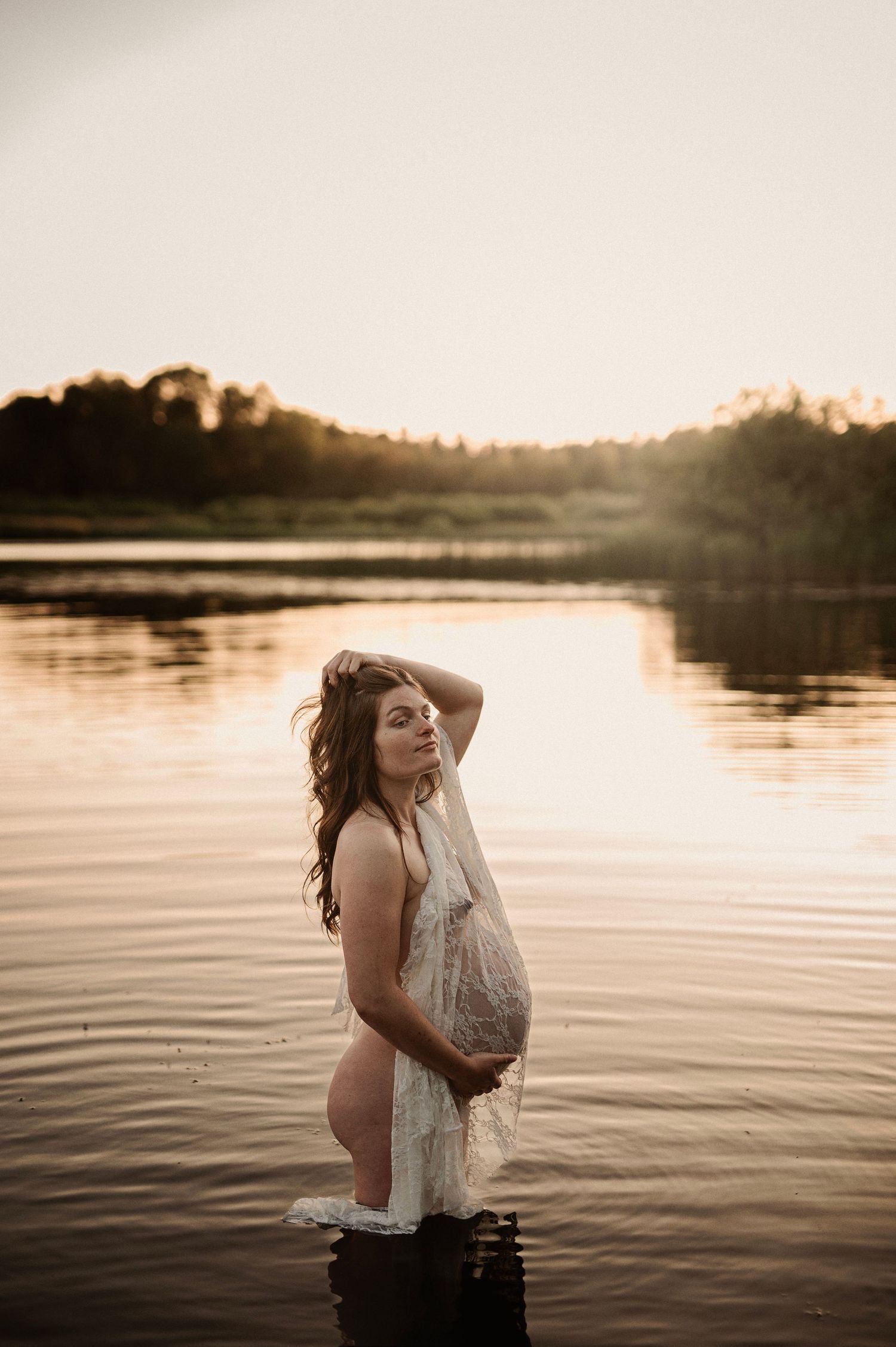Dreamy maternity portrait in water during golden hour sunset.