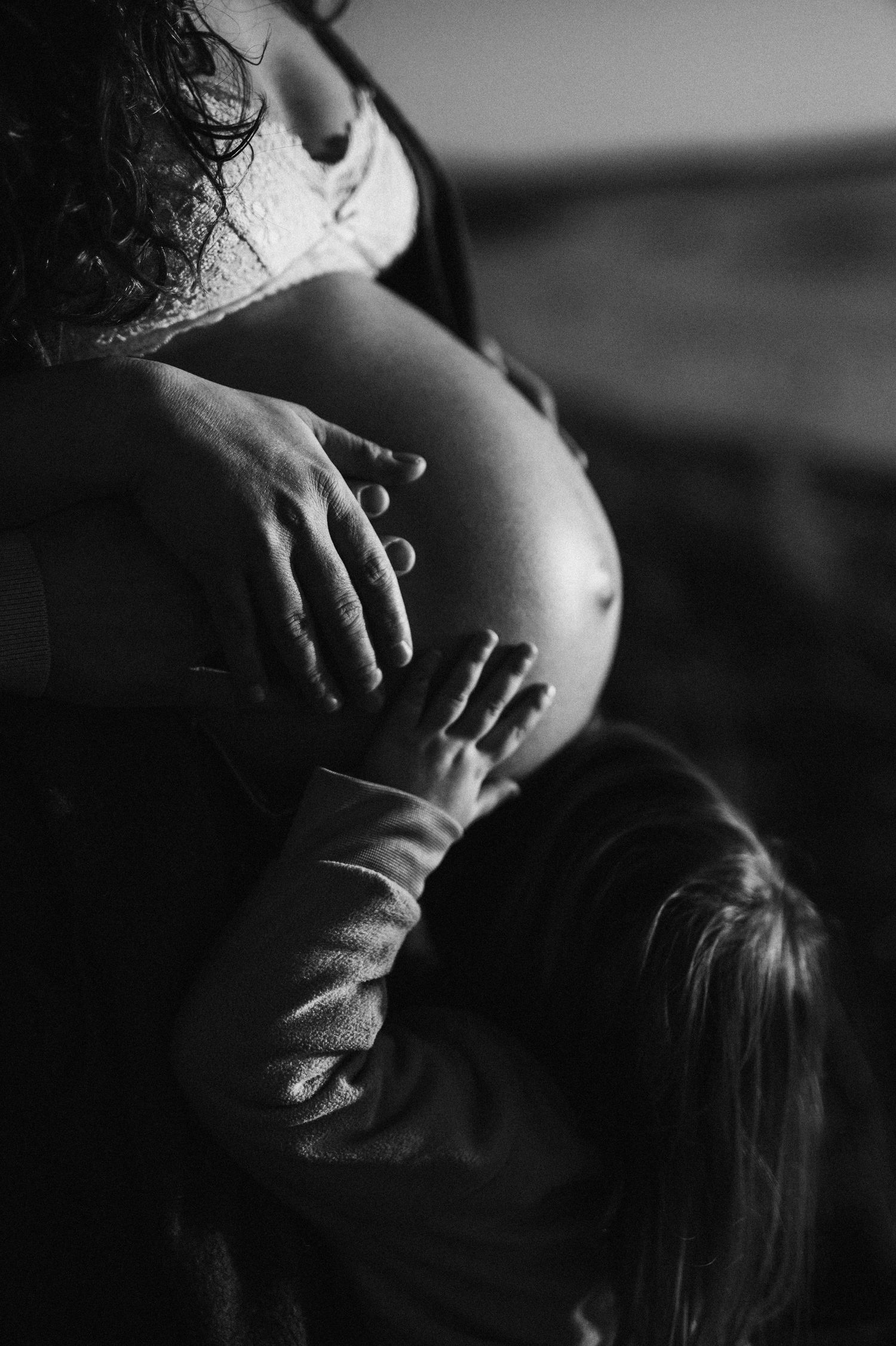 Black and white image of small hands touching a pregnant belly in intimate moment.